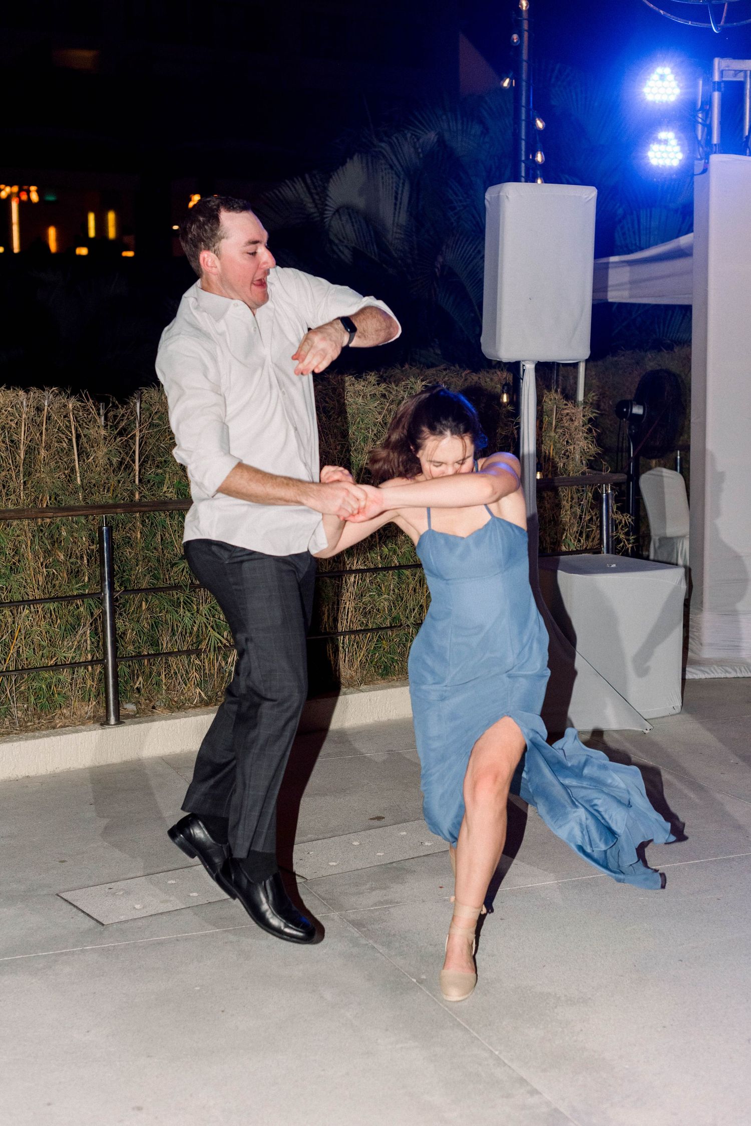 Couple performs energetic dance move at nighttime wedding celebration.