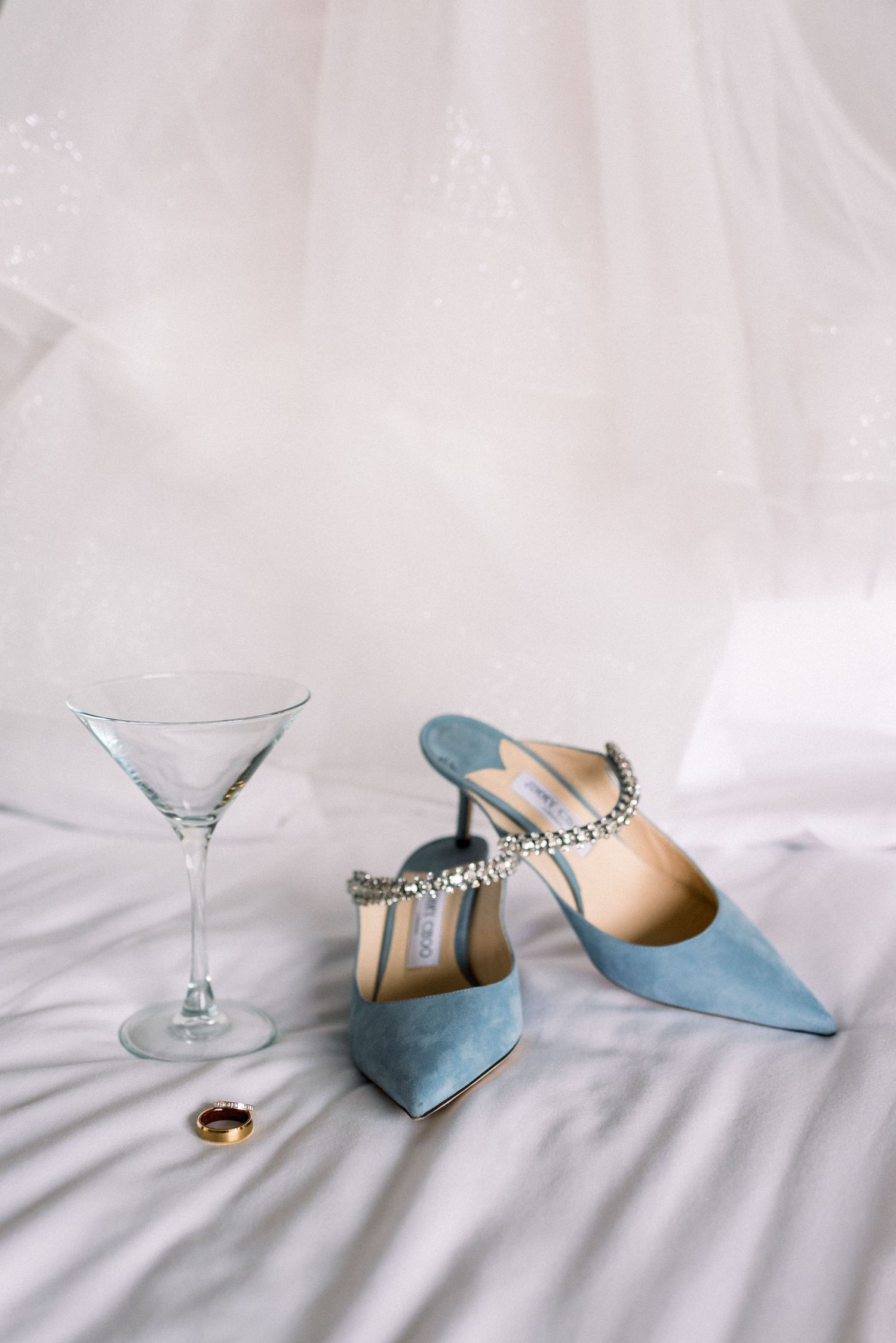 Elegant blue wedding shoes and martini glass arranged on white fabric.