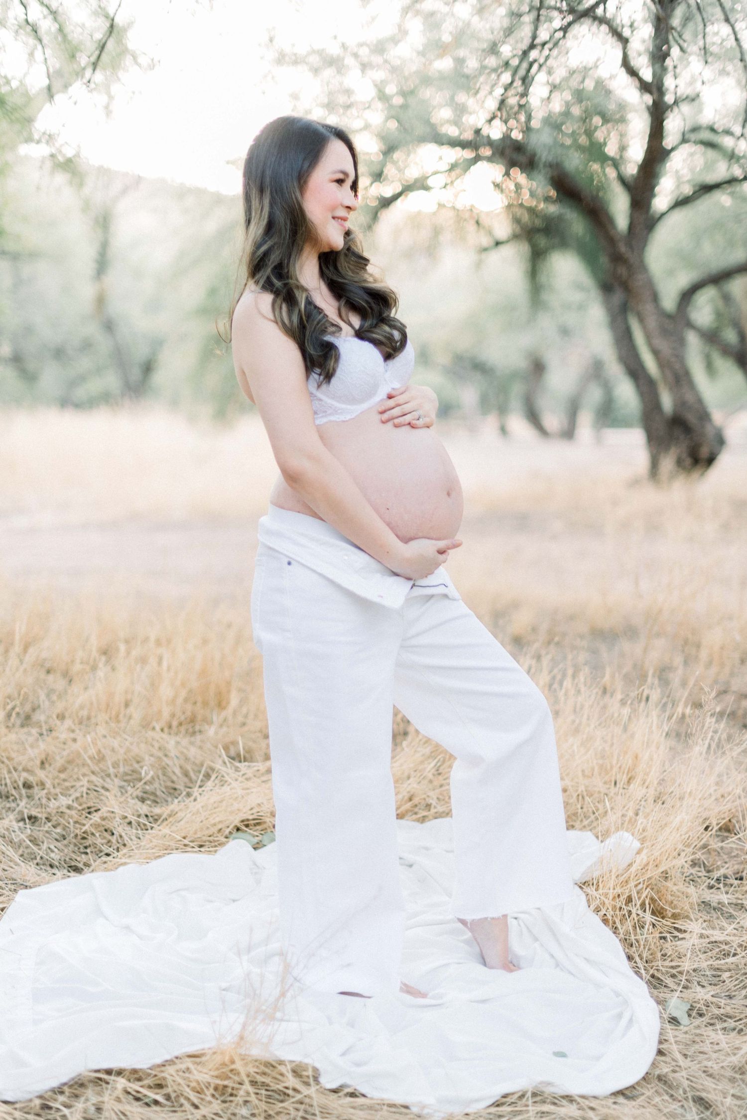 Elegant maternity portrait in white flowing dress against dried golden grass.