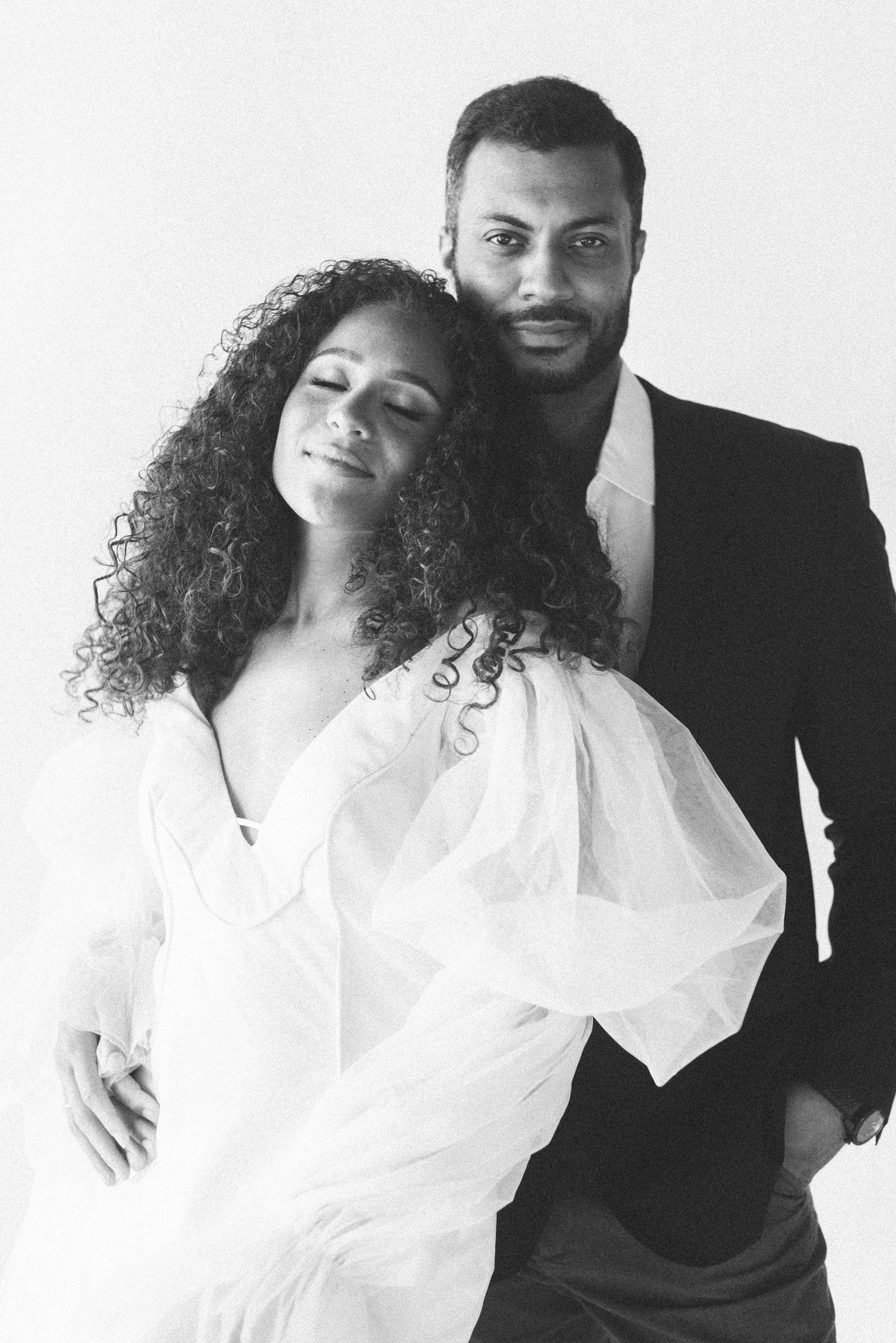 Black and white portrait of couple in romantic embrace wearing white and black outfits.