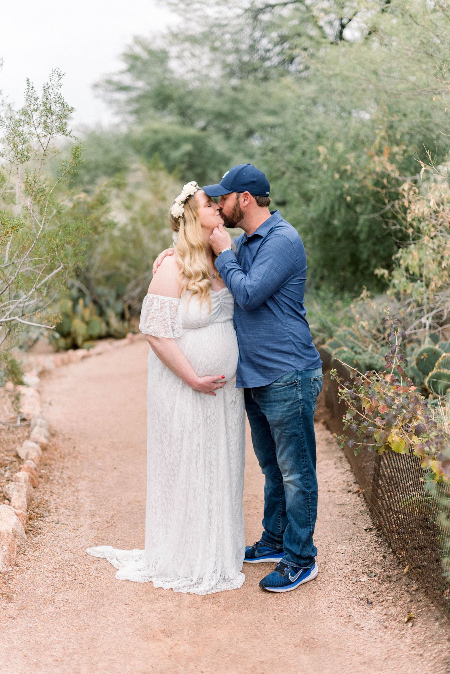 Romantic maternity photo of expecting couple sharing intimate moment on desert trail.