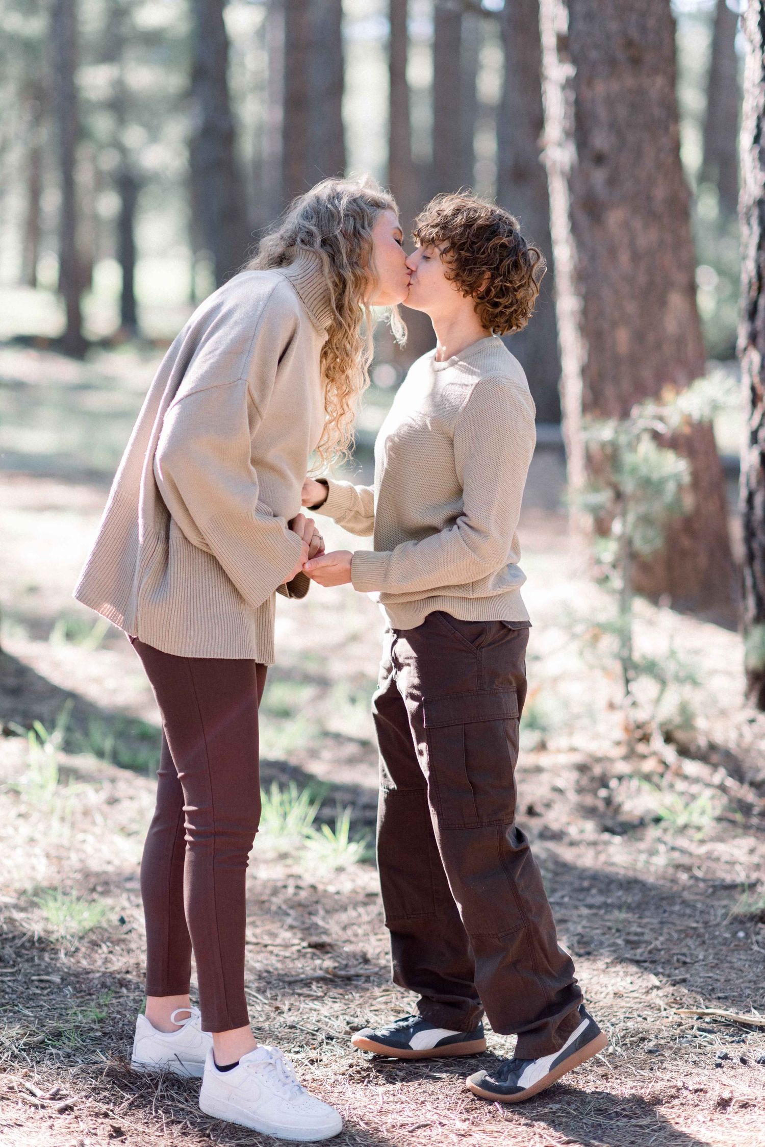Couple in neutral sweaters sharing romantic moment on forest path.