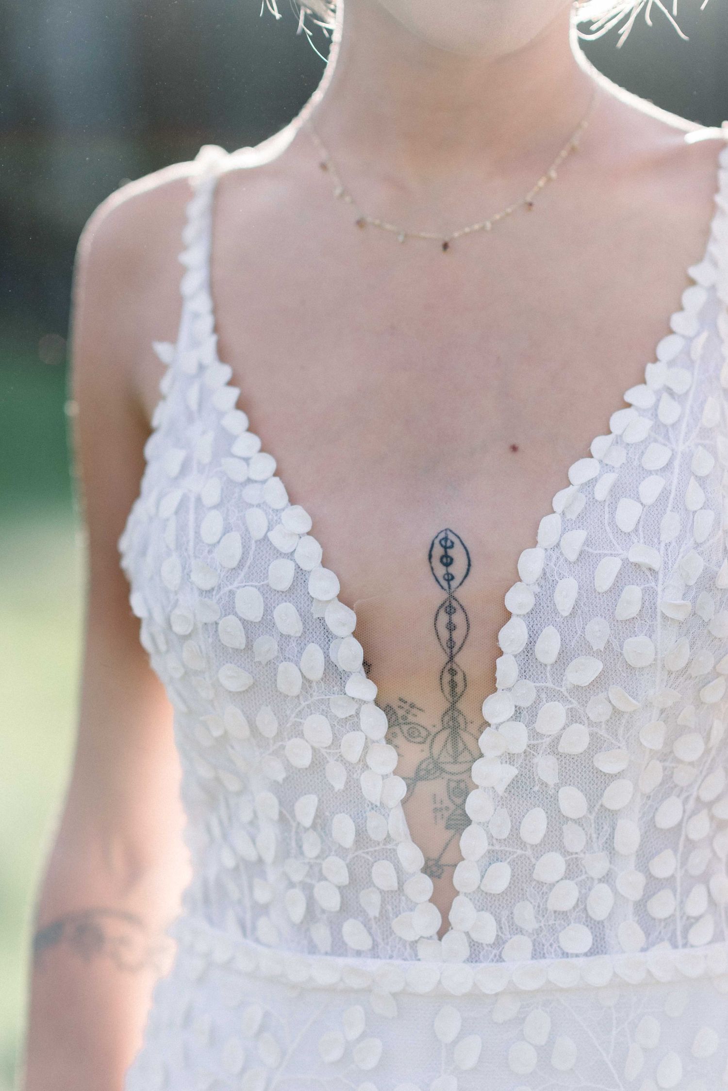 Close-up of white sequined wedding dress neckline with visible tattoo and dainty necklace.