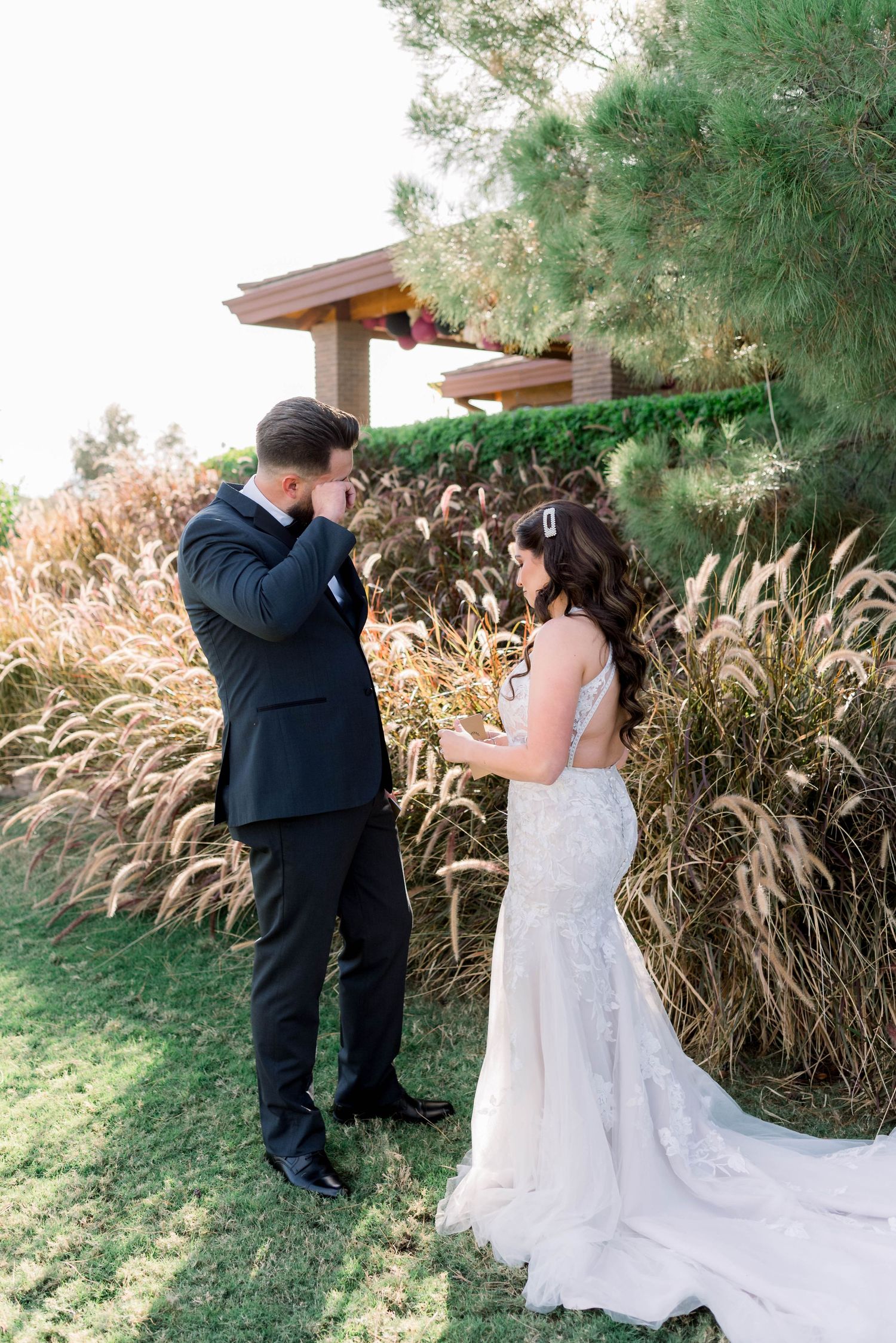 An emotional reaction during a wedding first look in a garden setting with decorative grasses.