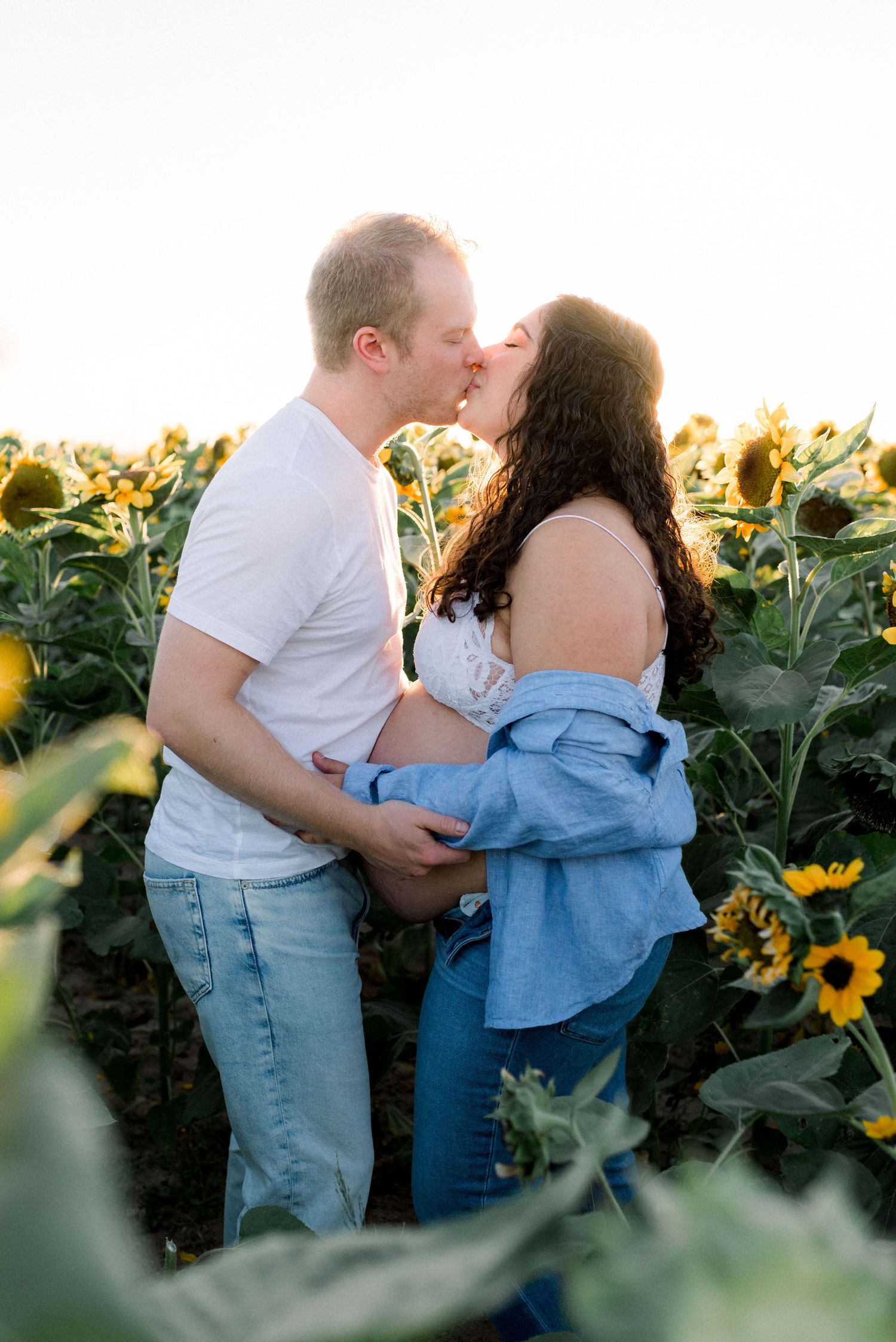 Maternity photo of couple kissing in sunflower field