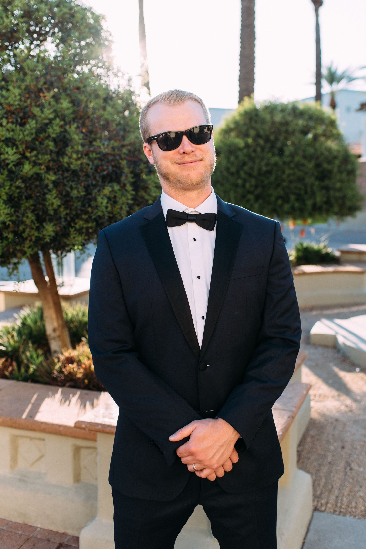A formal portrait of a man in classic black tuxedo and sunglasses standing outdoors.