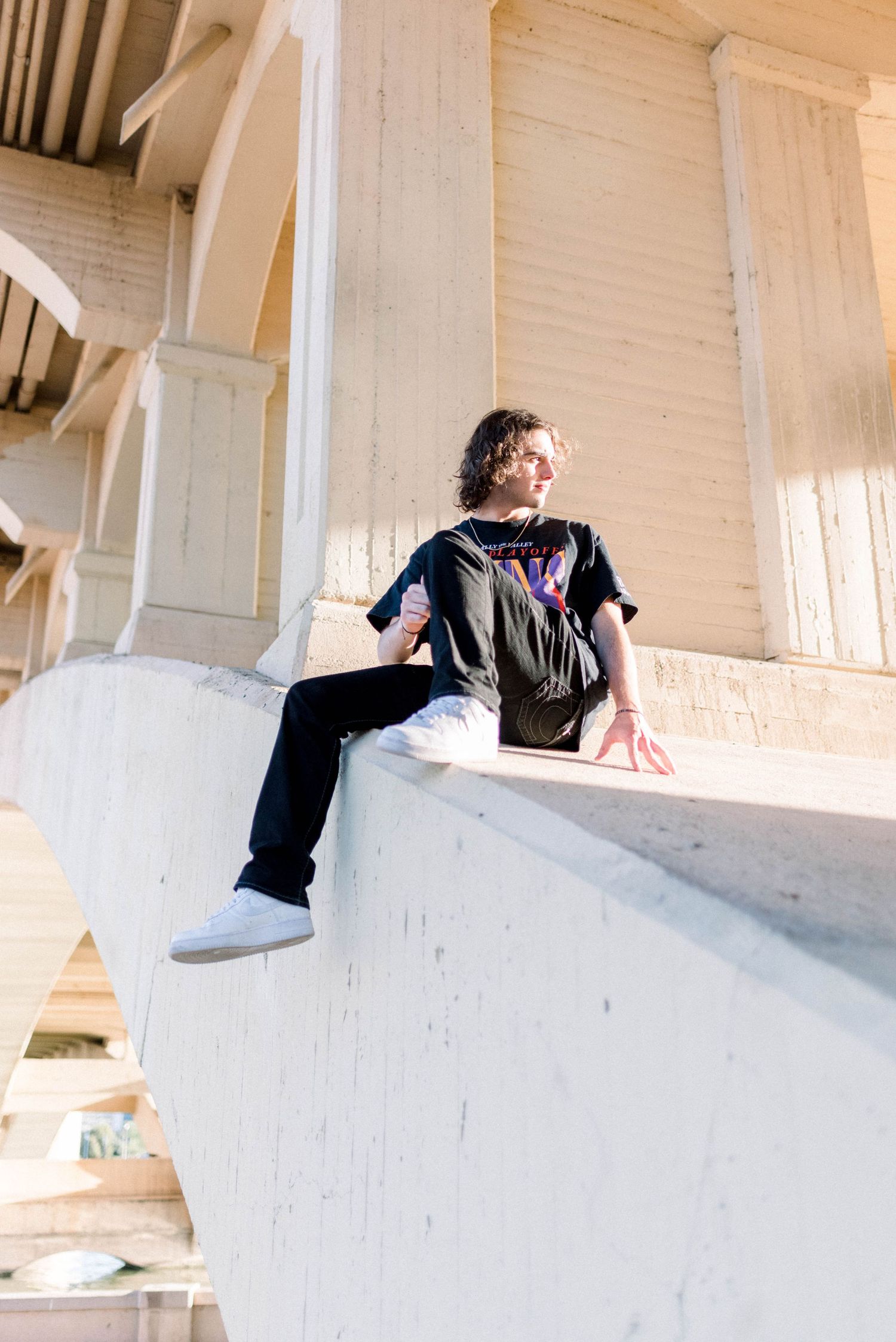 Person in casual wear sitting on white architectural ledge with sunlit backdrop.