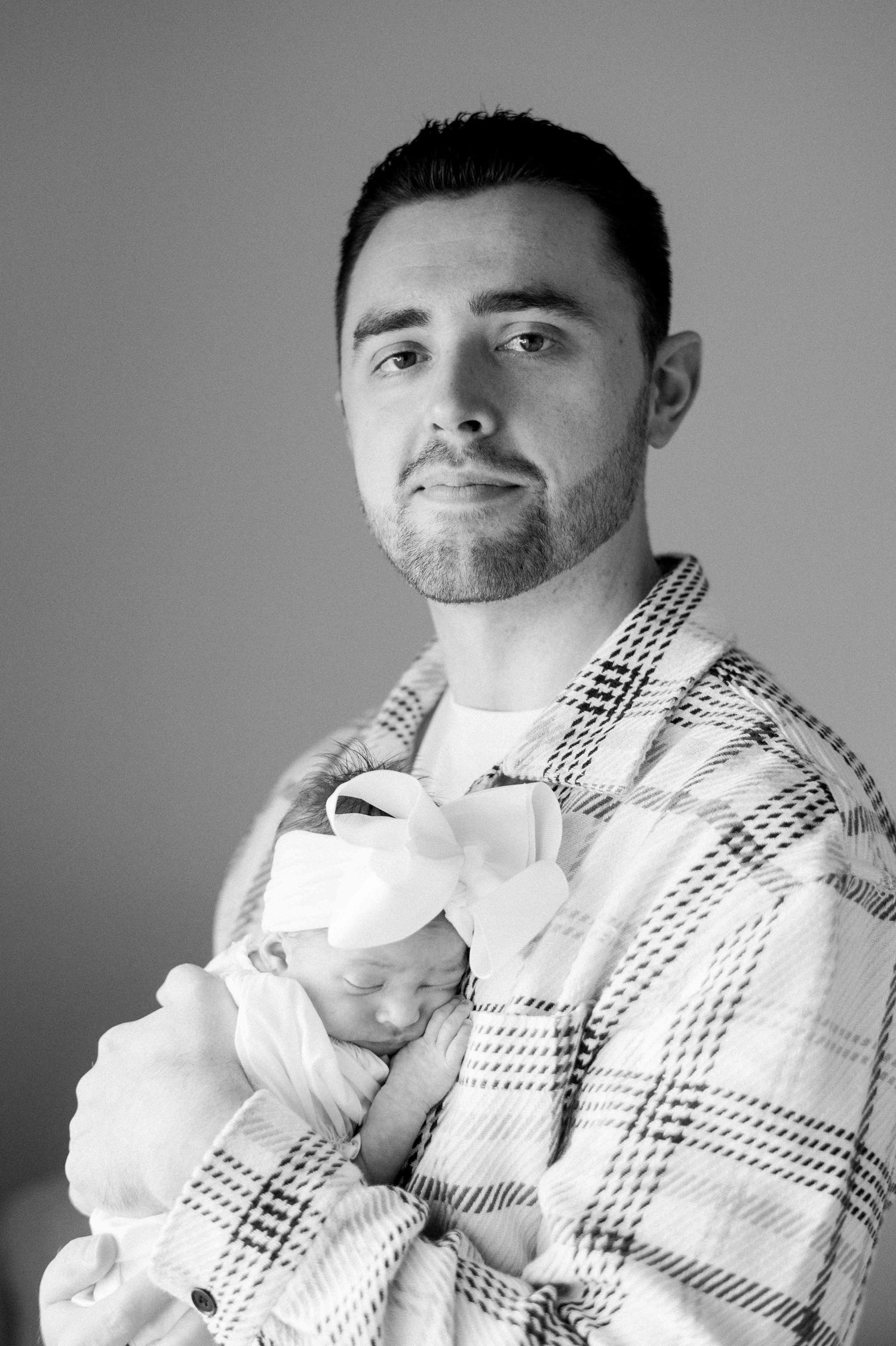 Parent in plaid flannel holds sleeping newborn in monochrome portrait.