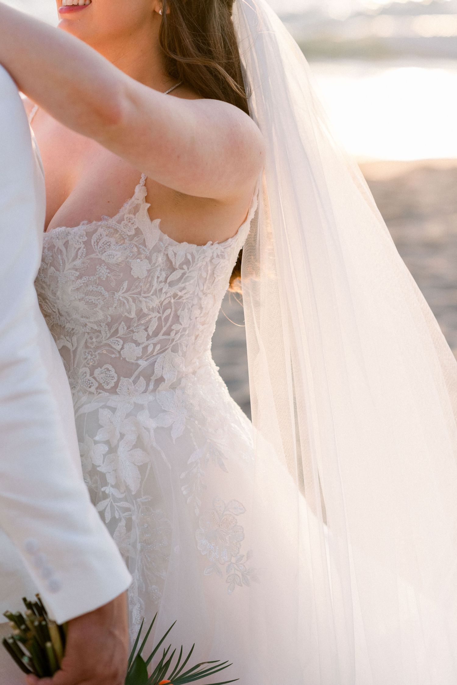 Detail shot of bride's lace wedding dress and flowing veil on beach.