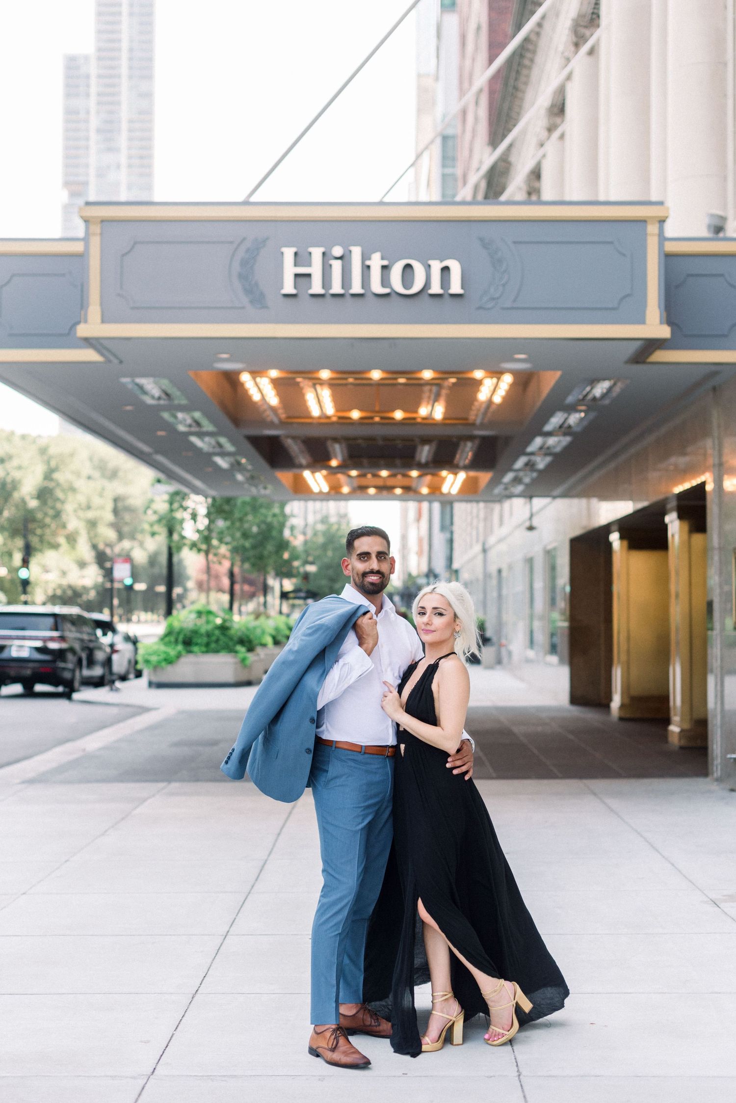Glamorous couple poses under illuminated Hilton hotel entrance.