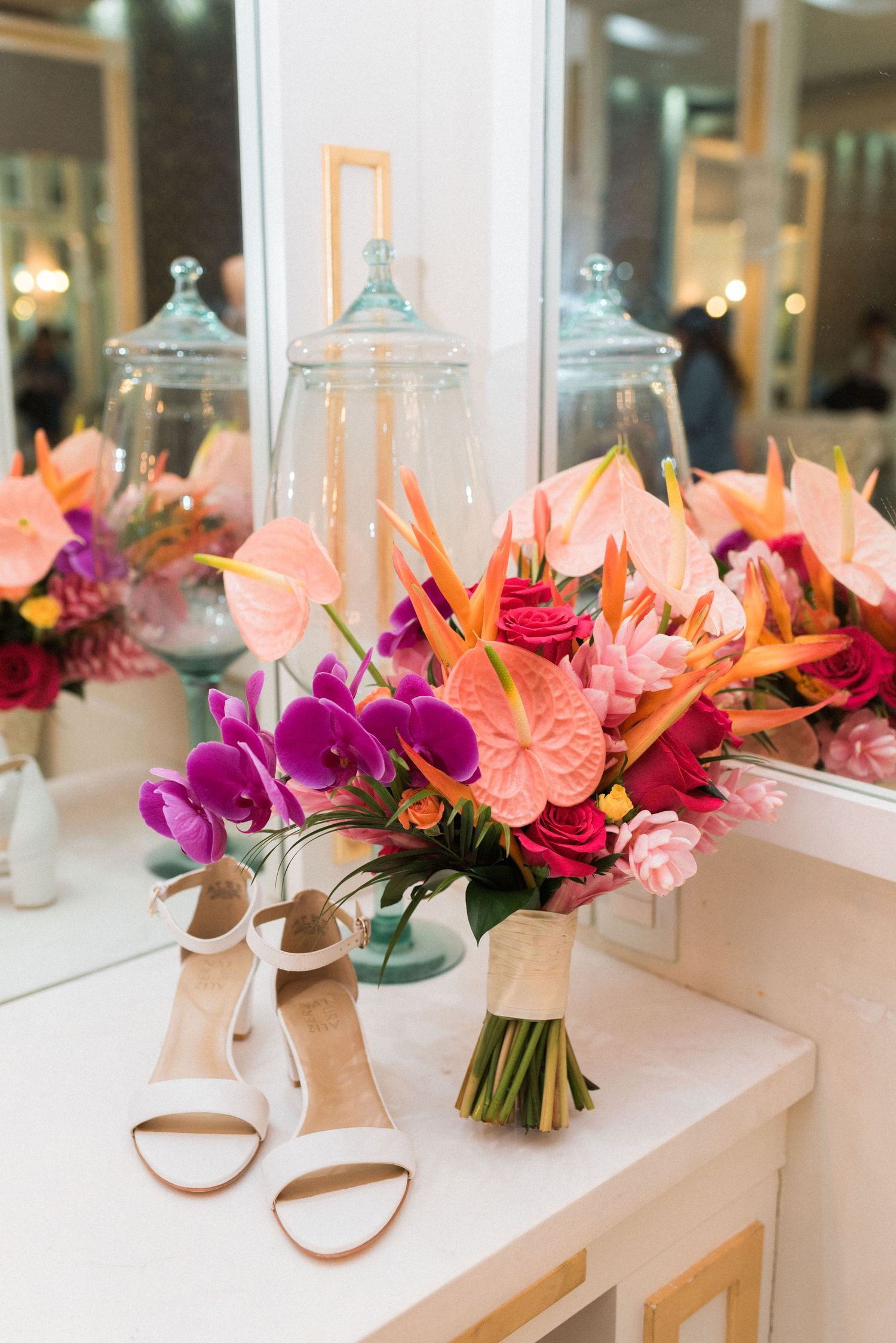 Elegant bridal bouquet with pink and purple flowers next to white sandals on a vanity with decorative lanterns.