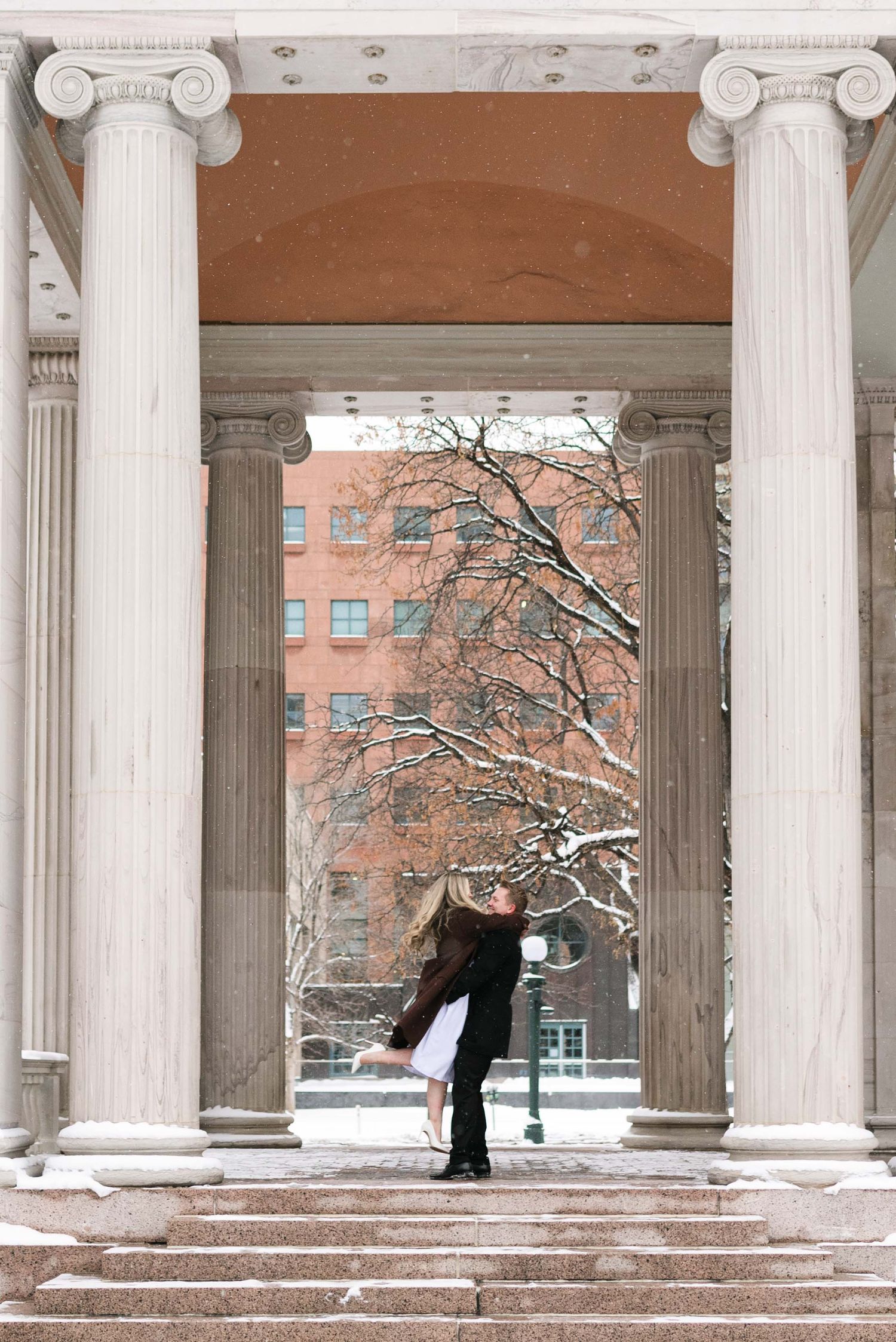 A romantic winter moment between two people framed by classical white columns.