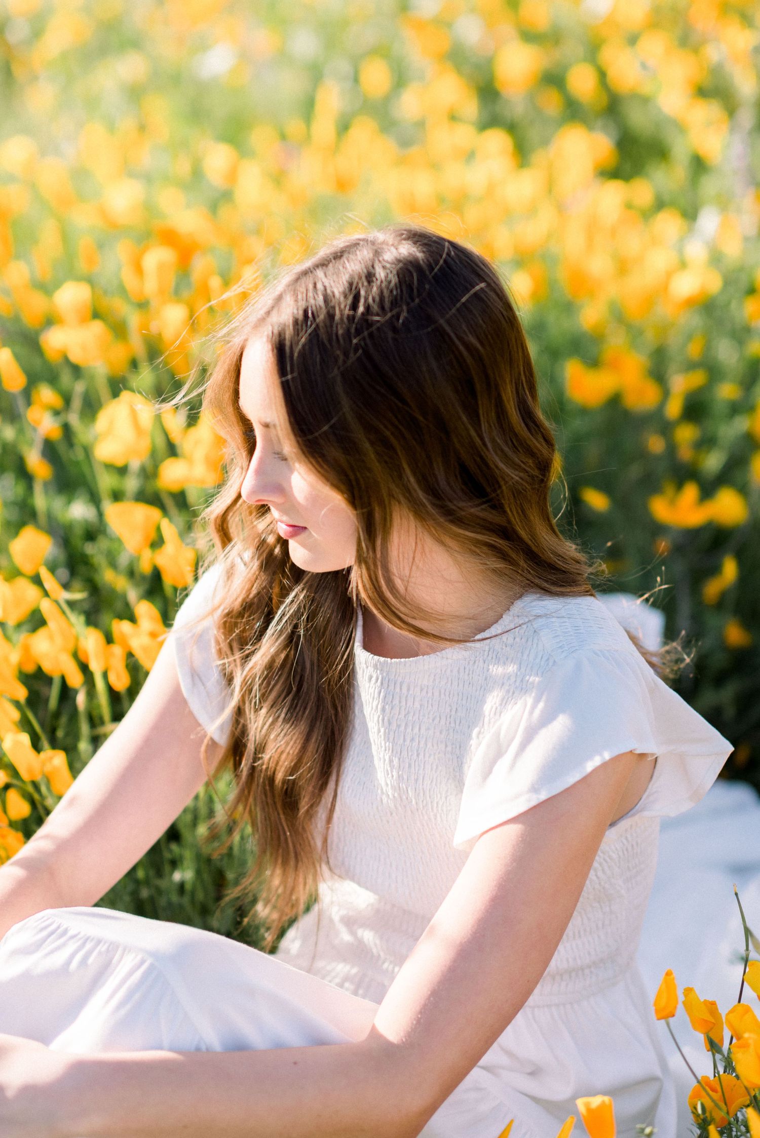White dress contrasts beautifully against vibrant yellow wildflower field in summer sunlight.