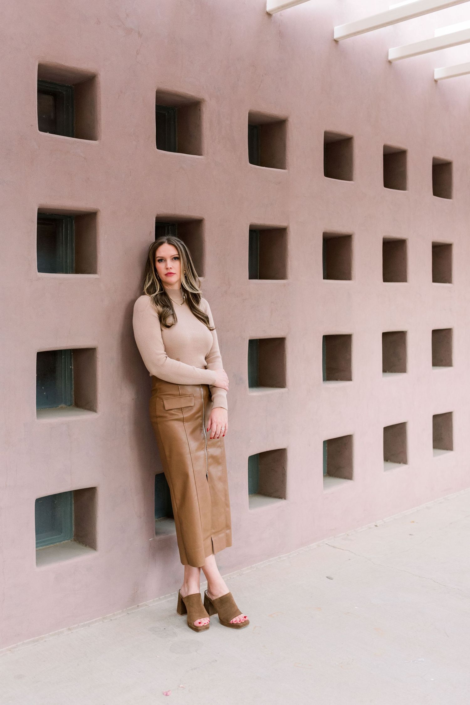 Fashionable outfit with beige sweater and tan midi skirt photographed against geometric wall design.