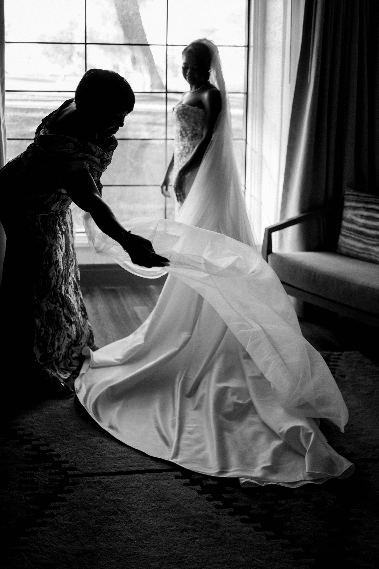 A black and white photo of a wedding dress being adjusted in front of a window.