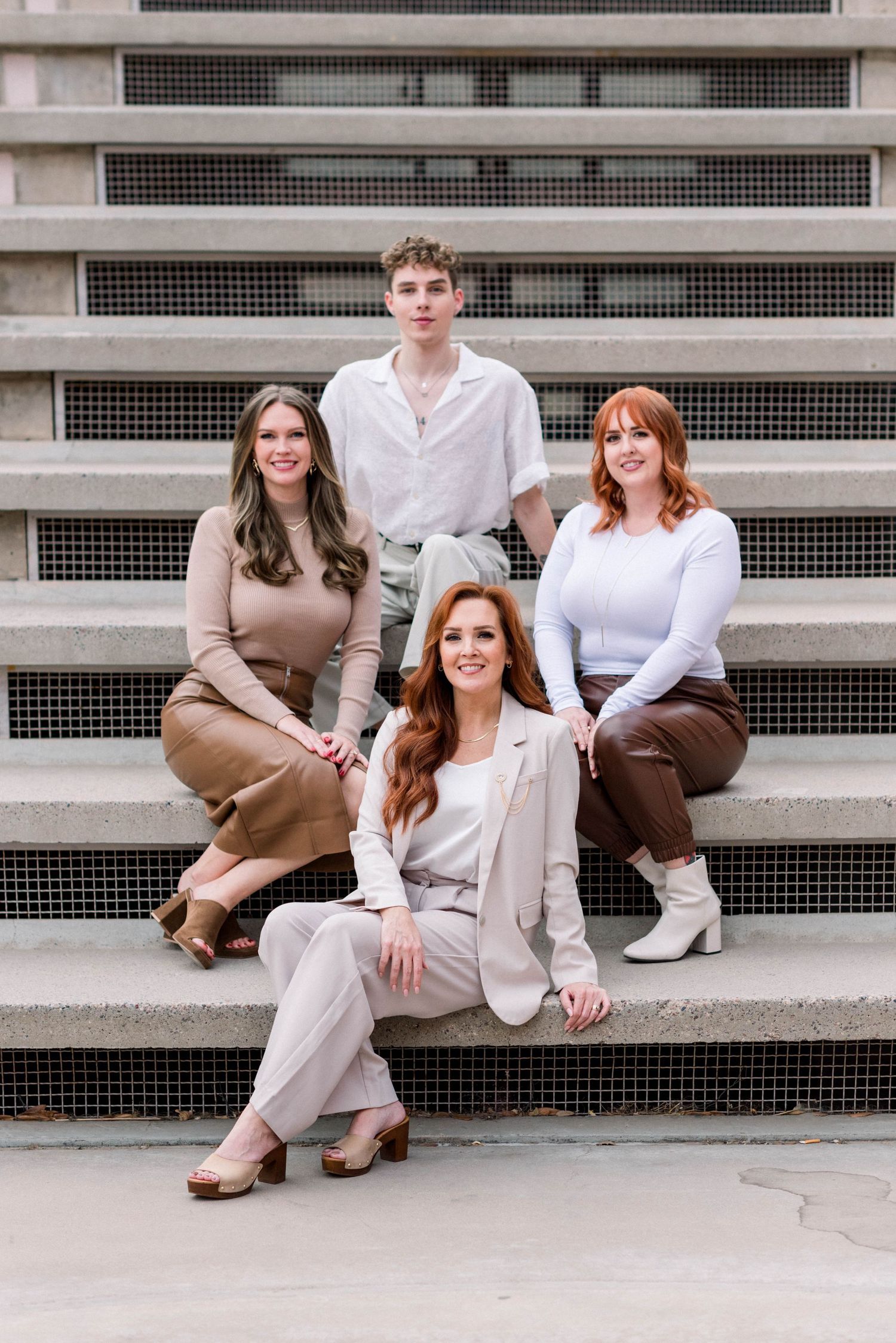 Group of people sitting casually on concrete steps wearing neutral toned outfits in a modern urban setting.