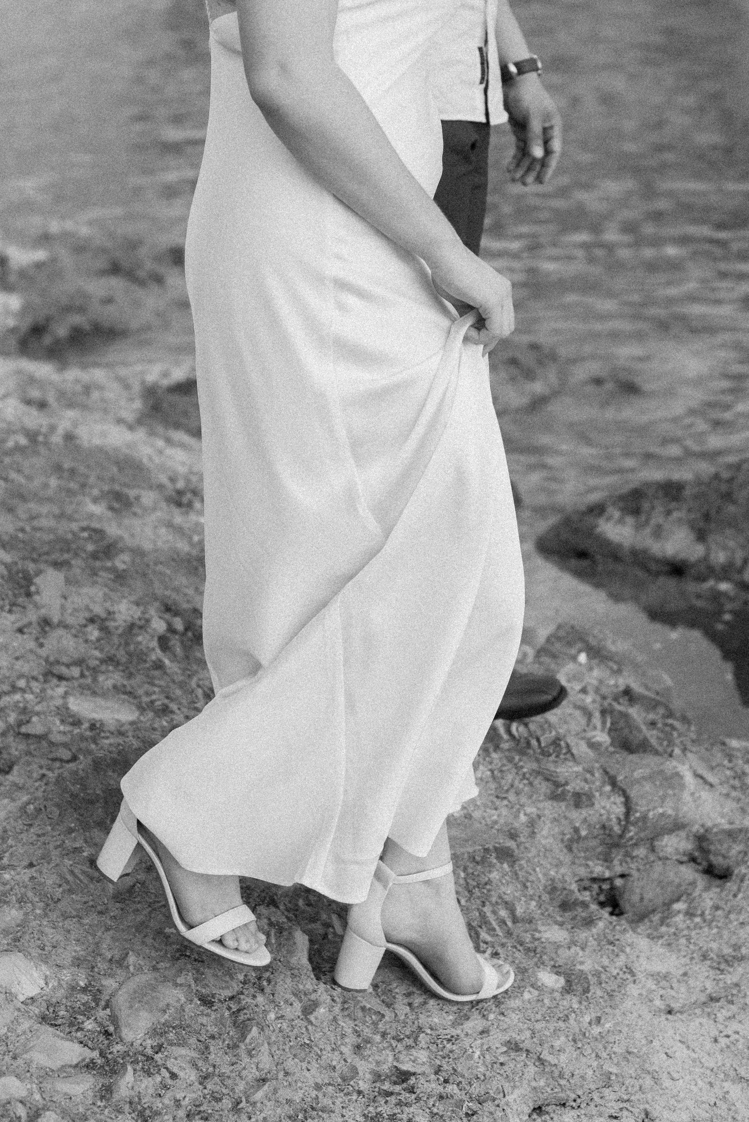 A close-up black and white photo shows feet in white heels walking carefully across rocky terrain.