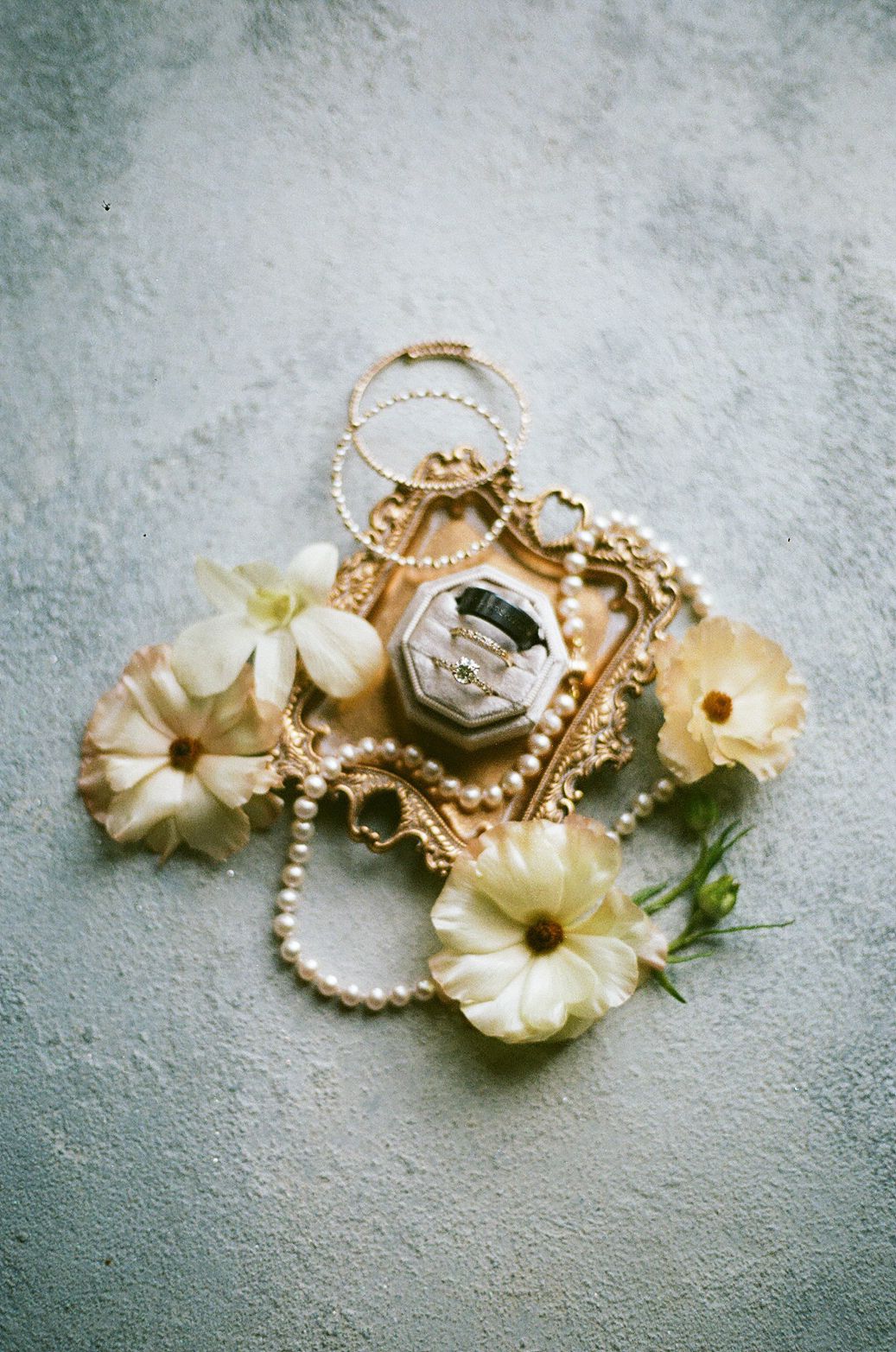 Wedding rings and delicate cream-colored flowers arranged on a textured gray surface.