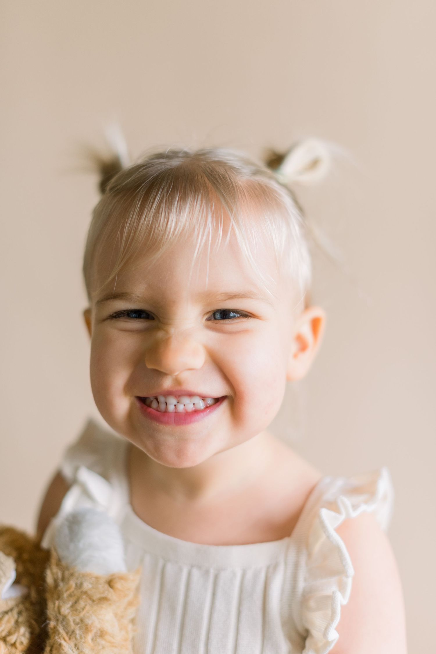 A joyful young child smiling brightly in white dress with hair styled in buns.