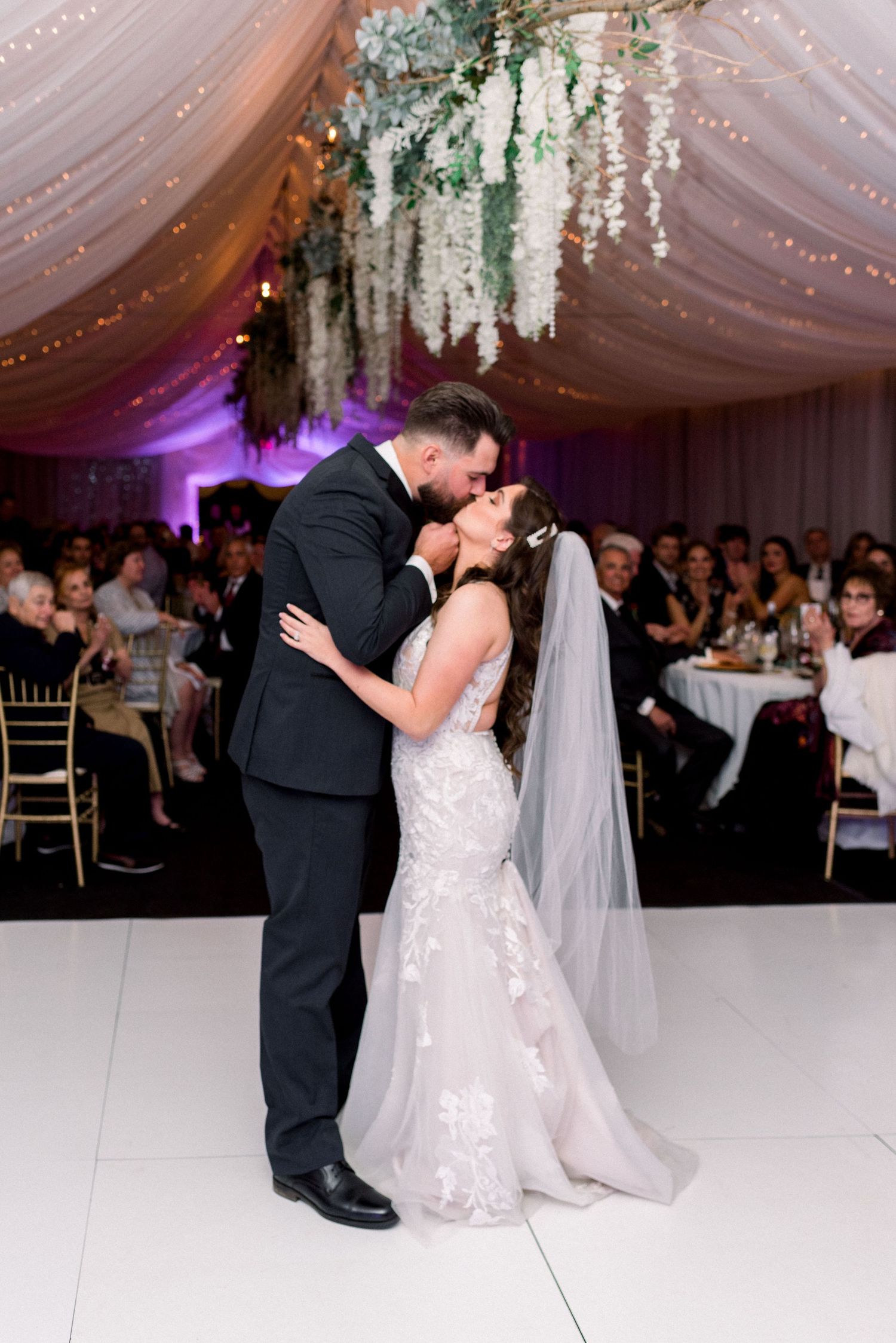 Couple shares romantic dance under hanging floral arrangements during their wedding reception.