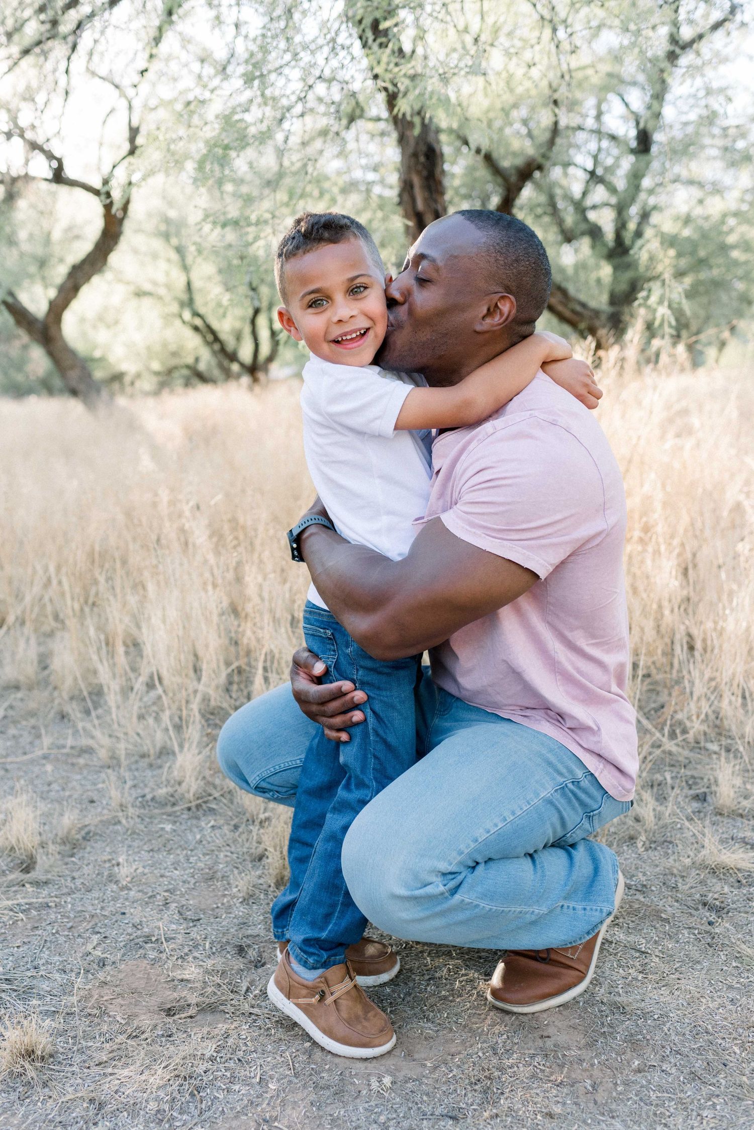 Tender moment between father and son hugging in outdoor setting with dried grass.