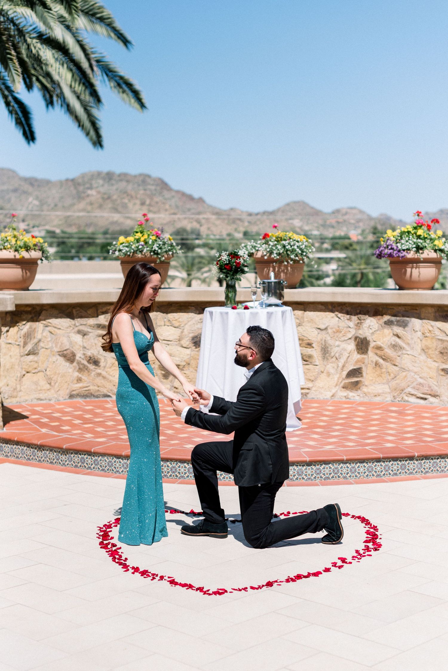 Marriage proposal moment on elegant terrace with mountain backdrop and red petal heart.