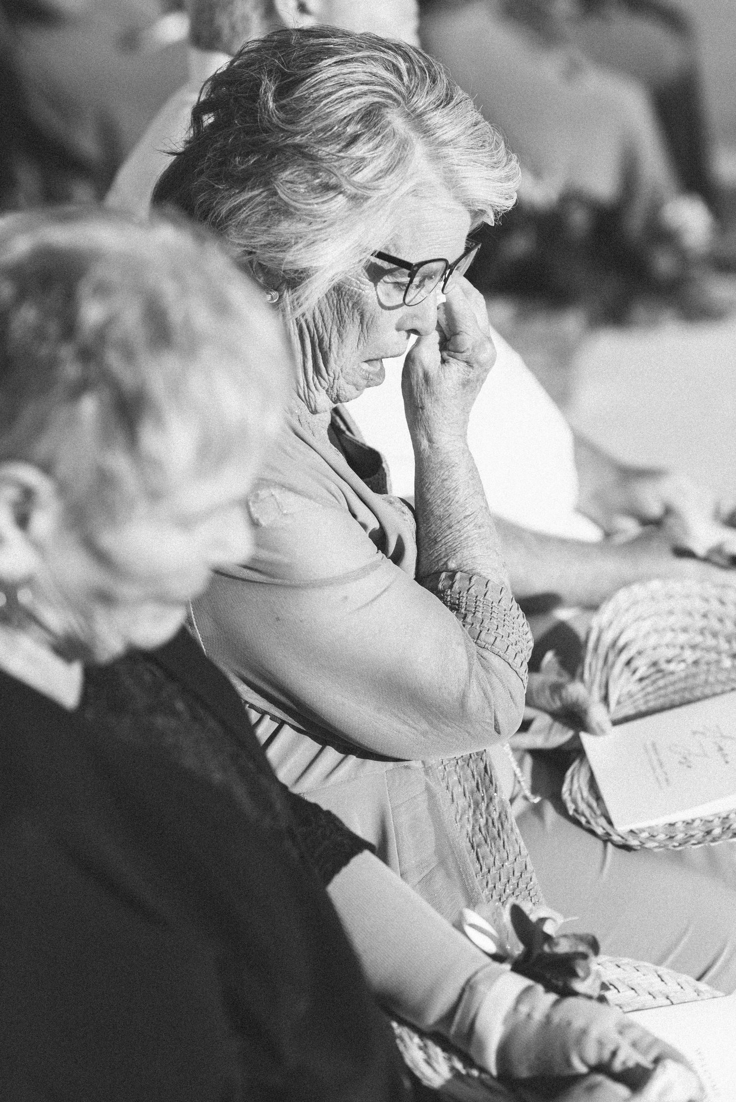 Black and white photo of emotional wedding guest wiping tears during ceremony.