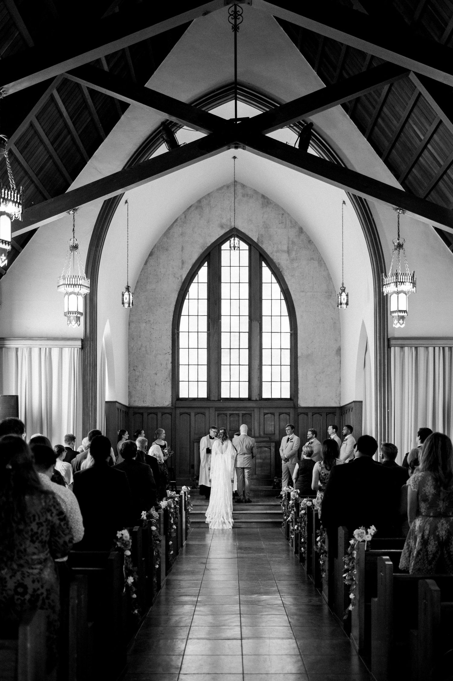 Black and white photo of traditional church wedding ceremony with gothic arched windows.