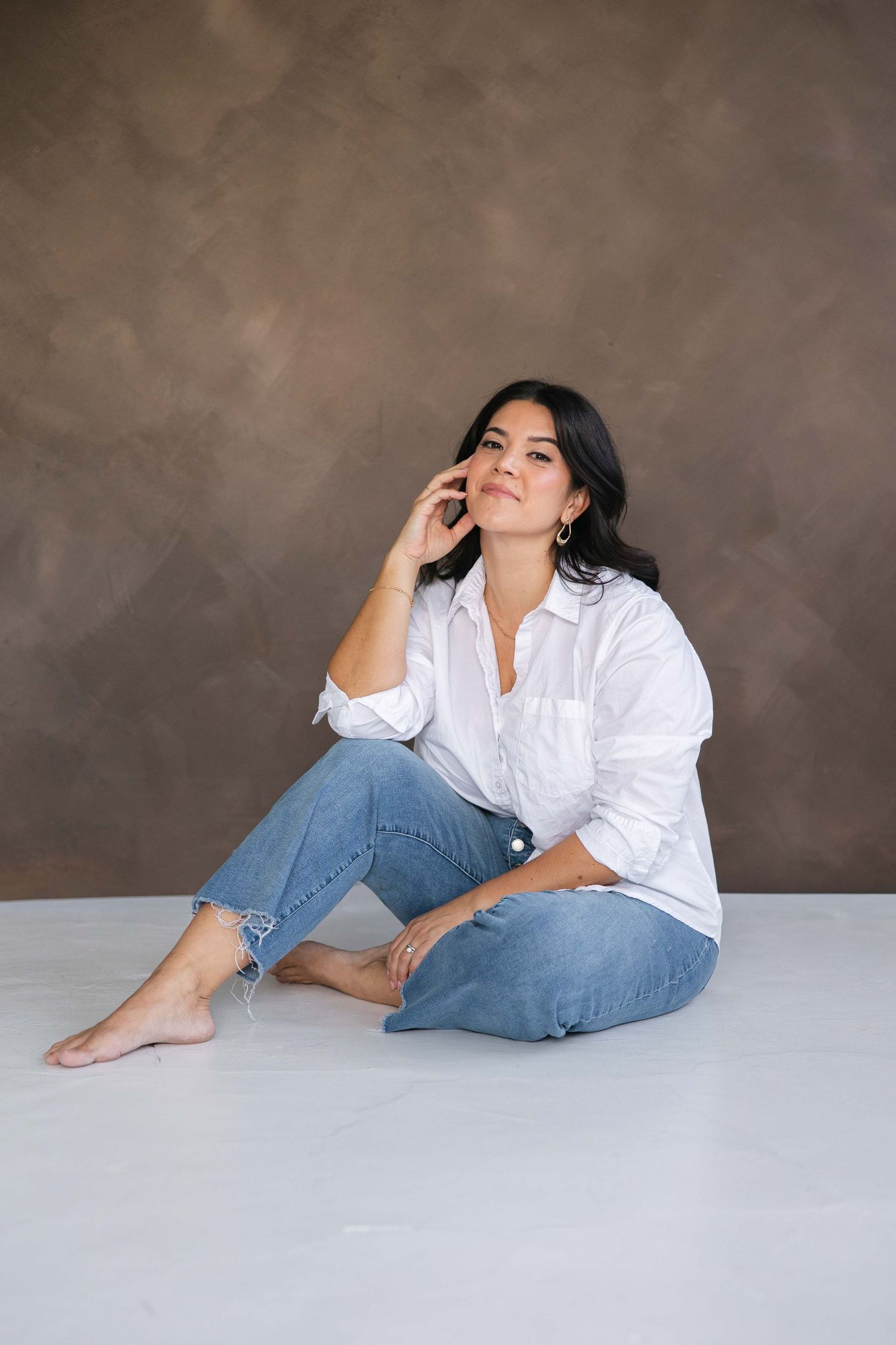 Lifestyle photography poses in classic white button-down and jeans on light surface.