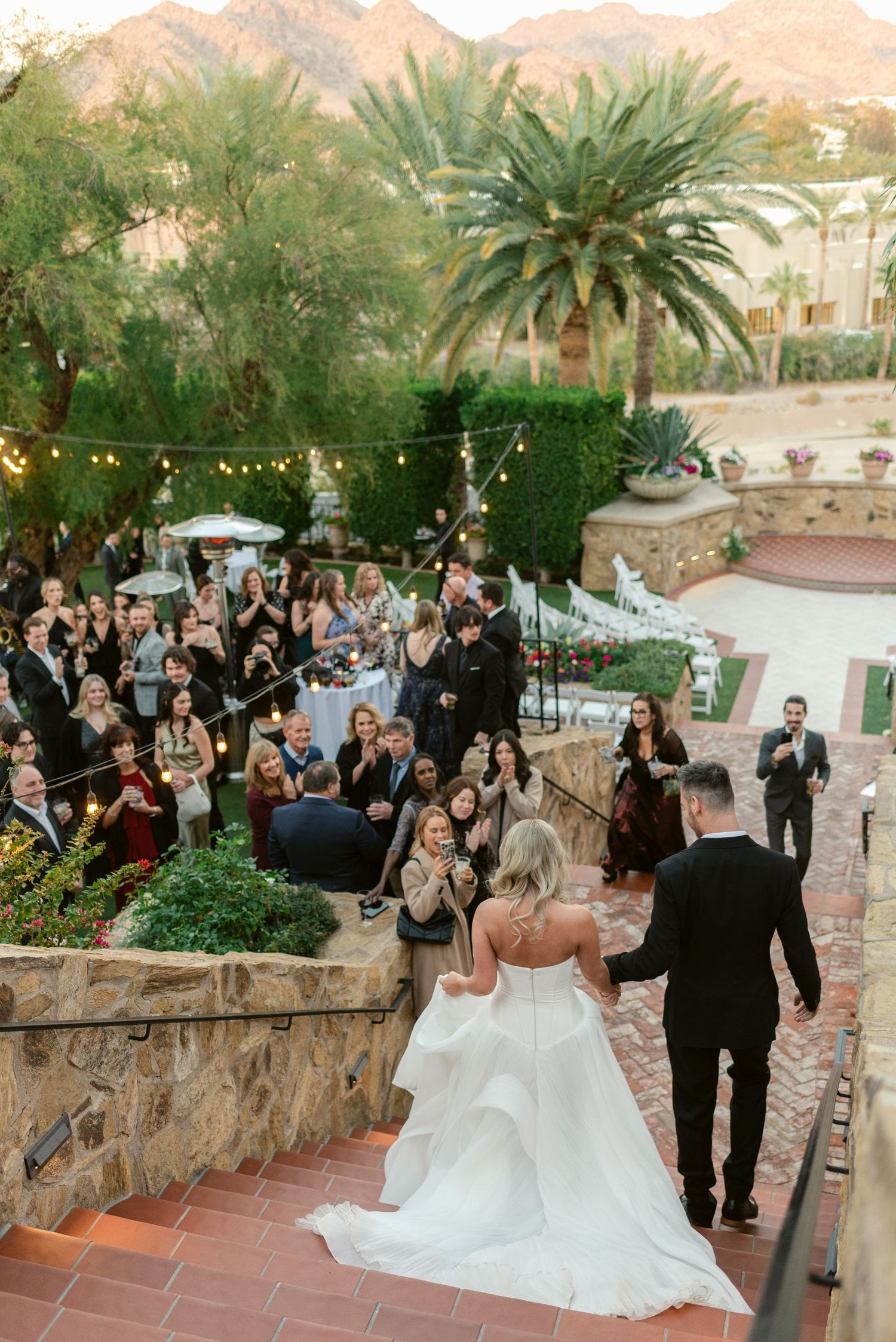 Wedding celebration at sunset with mountain views and string lights in an outdoor desert venue.