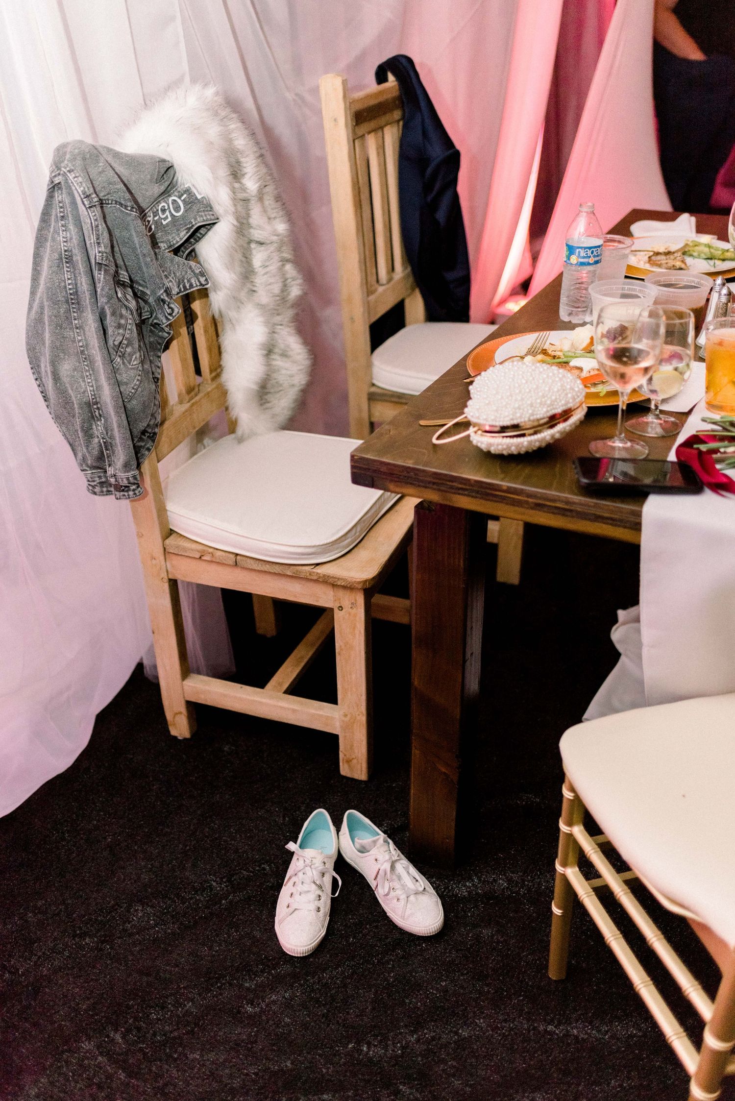 A fur-trimmed jacket and white sneakers rest near a wooden chair at a wedding reception.