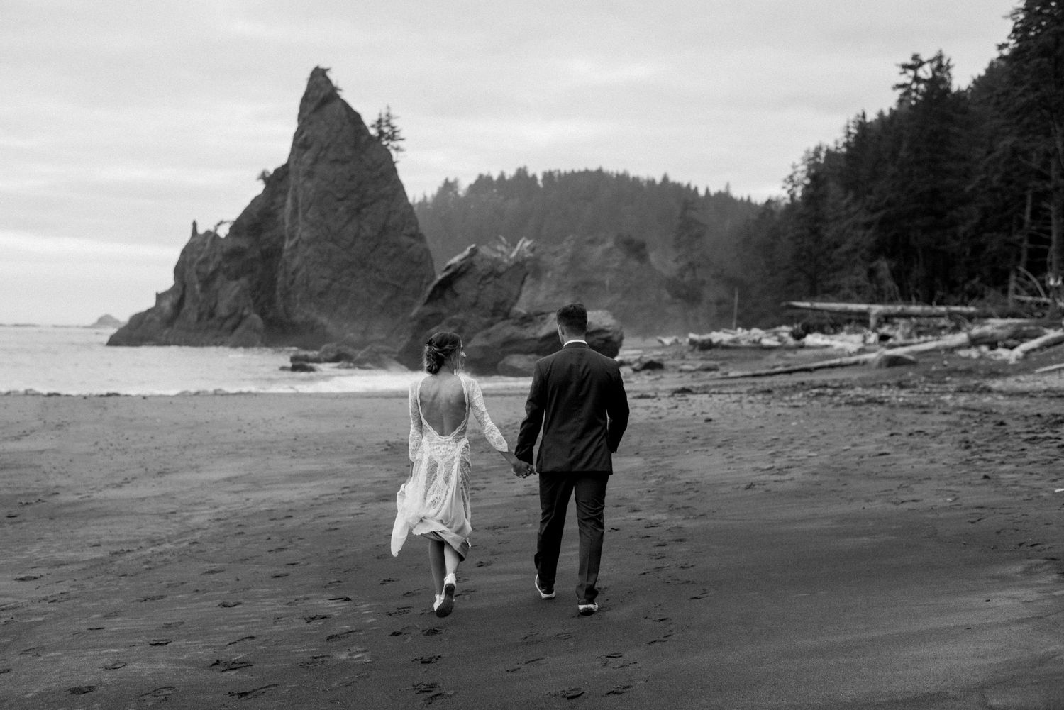 A couple walks hand in hand along a misty beach with dramatic coastal rock formations.