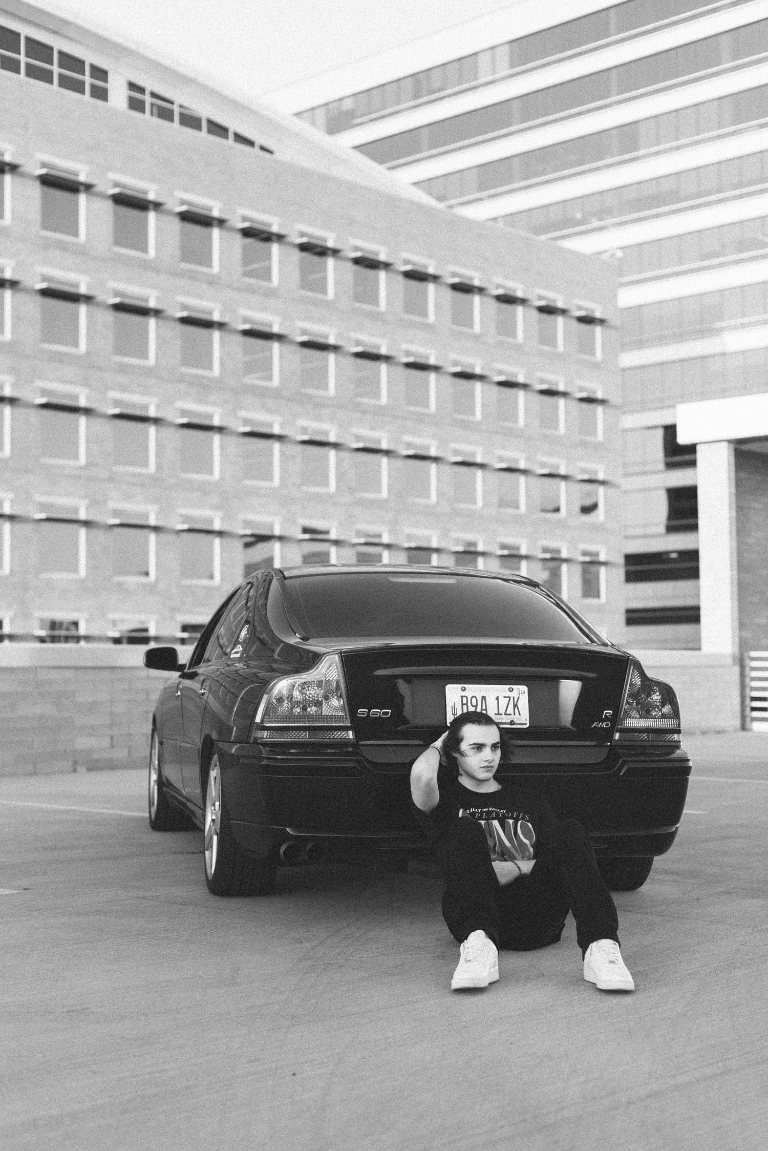 Person sitting against black sedan in parking structure.