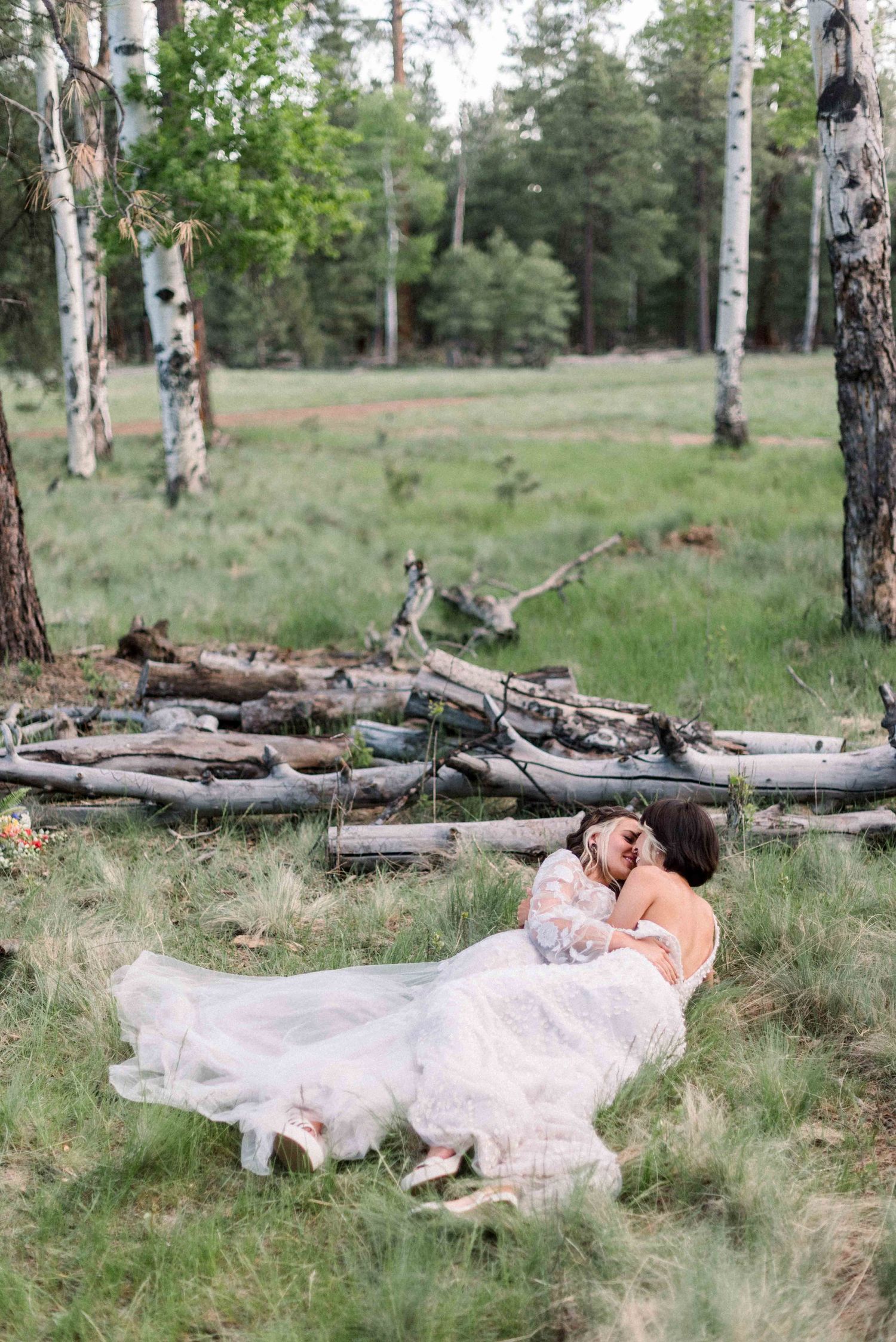 A loving couple in white dresses embrace among birch trees in a forest setting.
