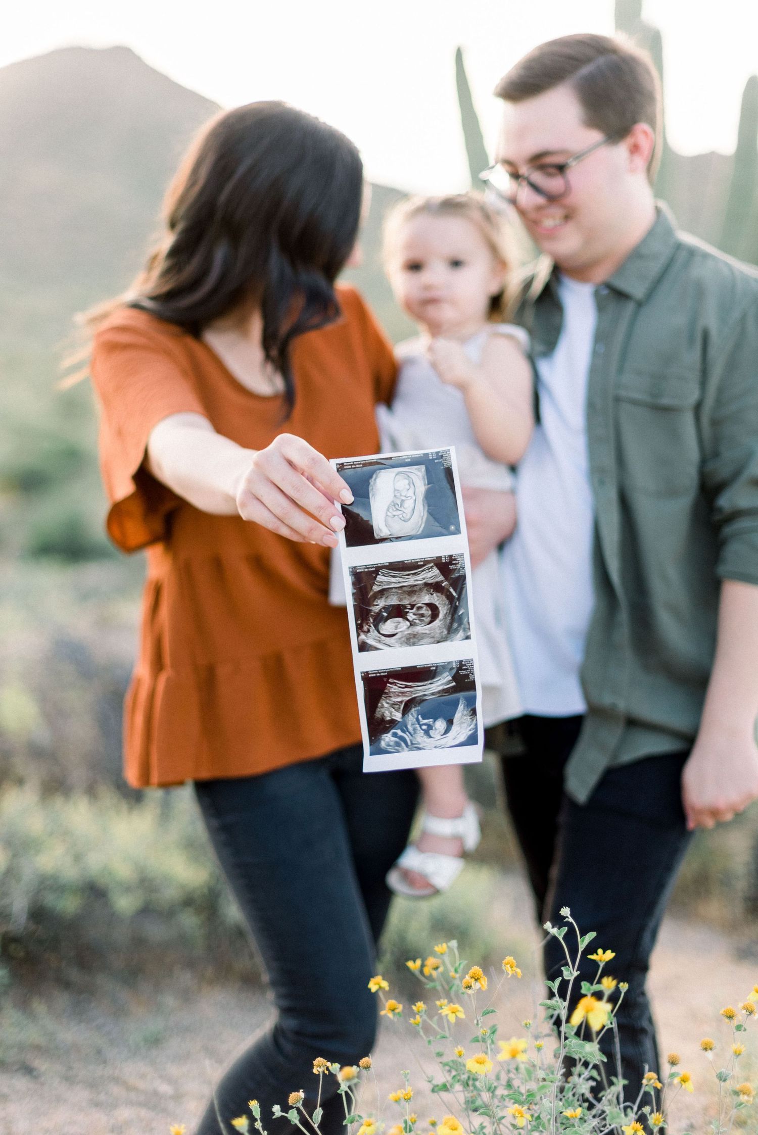 A pregnancy announcement photo with sonogram images displayed in desert setting.