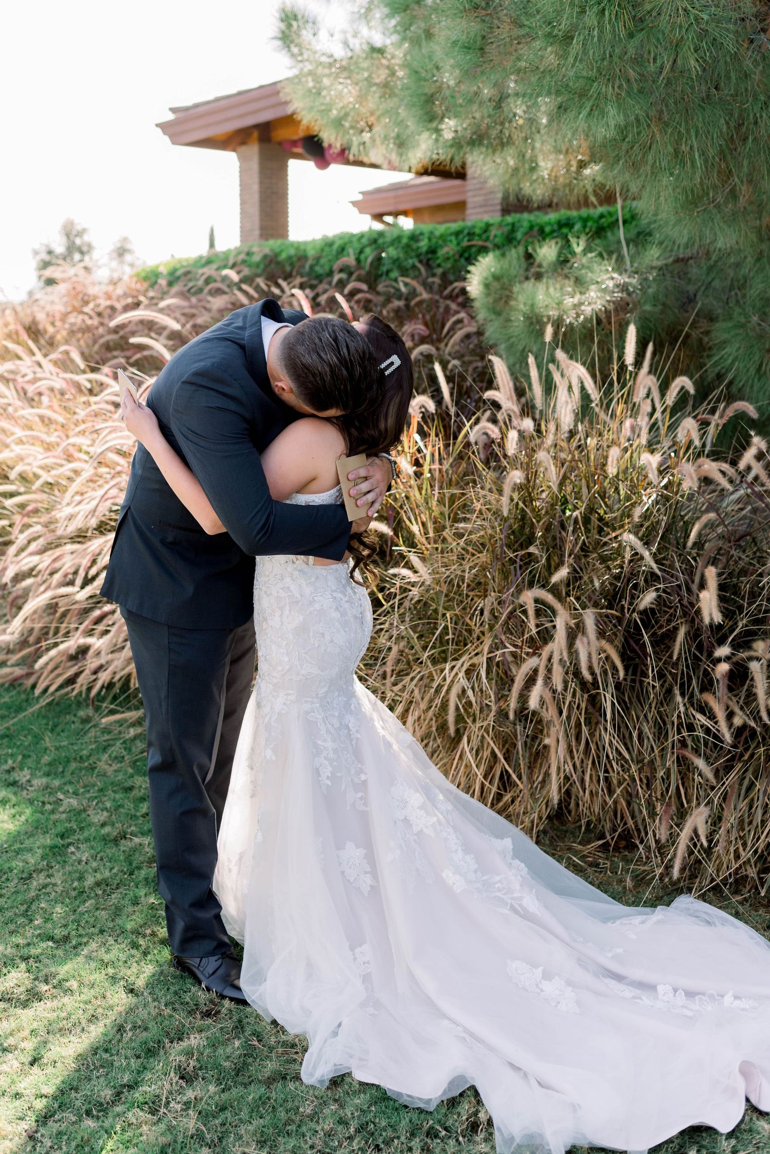 A couple embraces during their outdoor first look moment against a backdrop of ornamental grasses.
