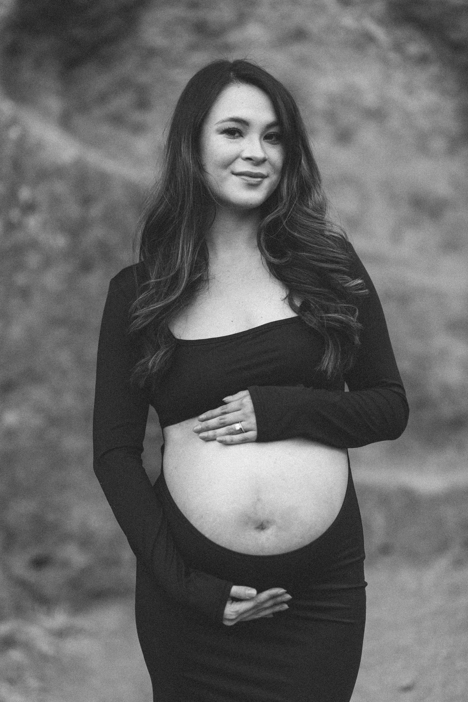 Black and white maternity photo of an expectant mother in long sleeve dress cradling her baby bump.