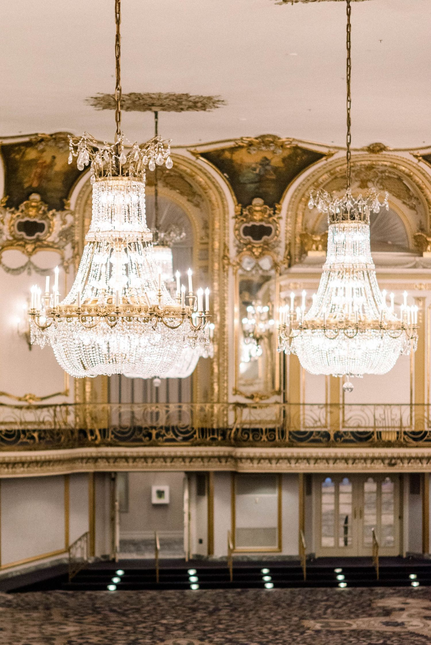 Two magnificent crystal chandeliers hanging in a grand ballroom with ornate ceiling details.