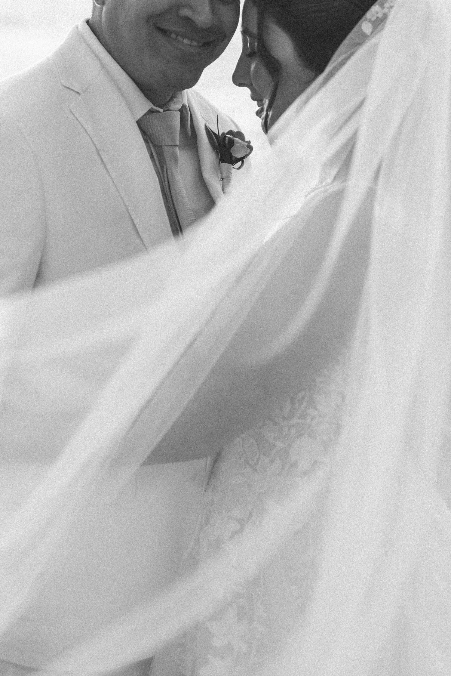 Black and white close-up of couple sharing tender moment under veil.