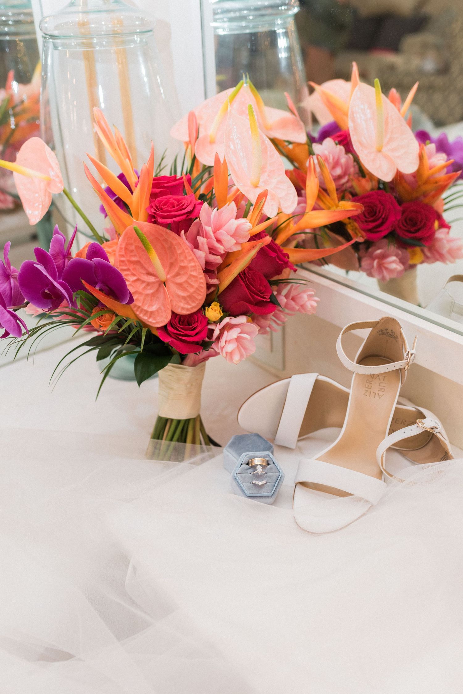 Vibrant tropical bridal bouquet with anthurium and roses next to white wedding shoes.