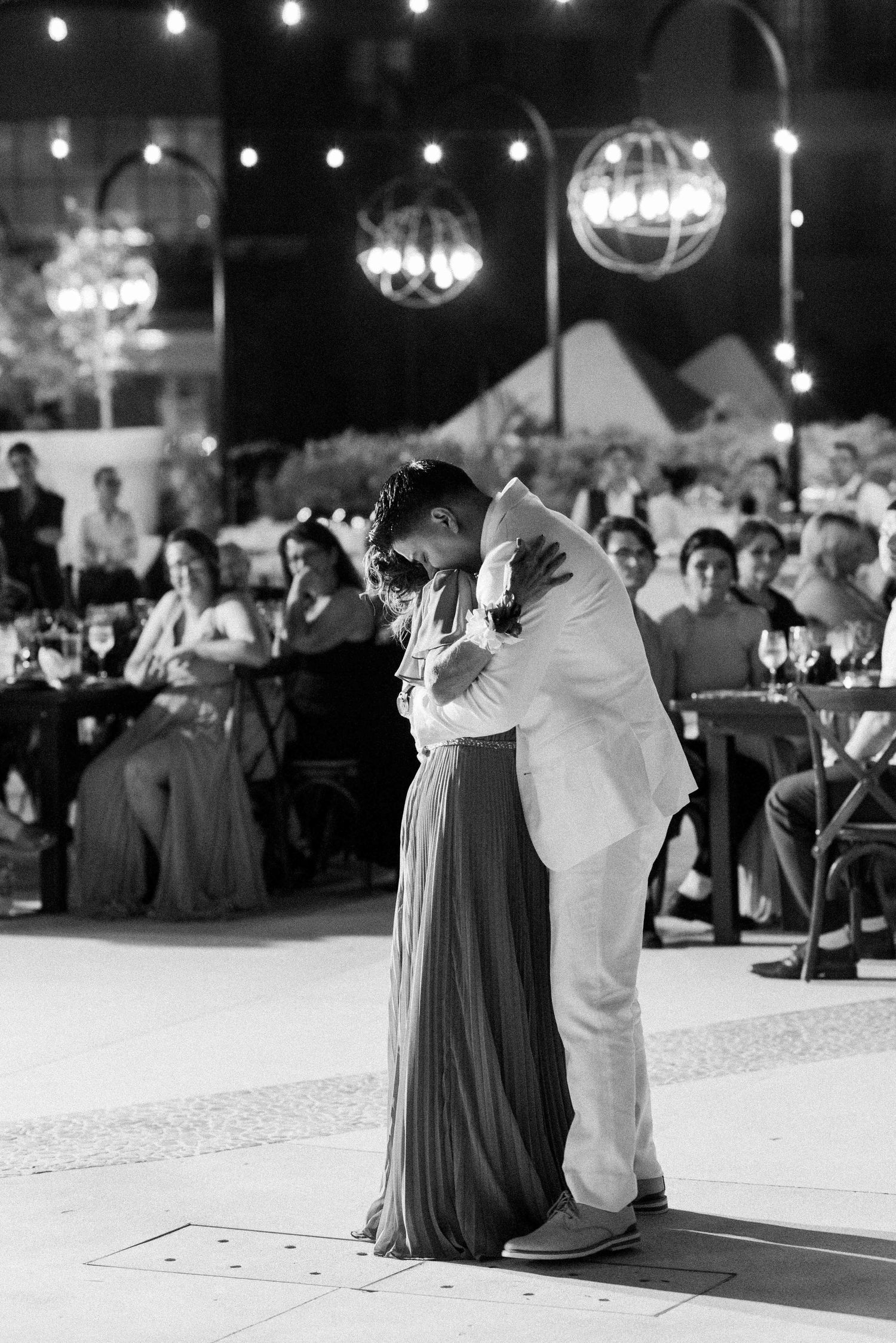 A couple shares an intimate dance moment under string lights at their wedding reception.