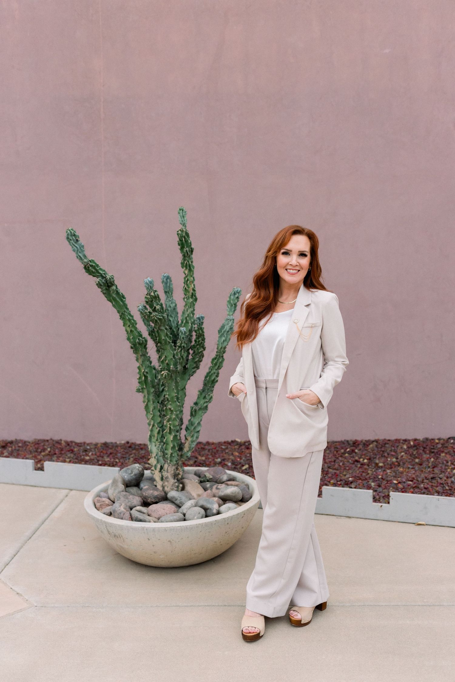 Stylish cream colored suit ensemble posed next to modern landscaping with cactus.