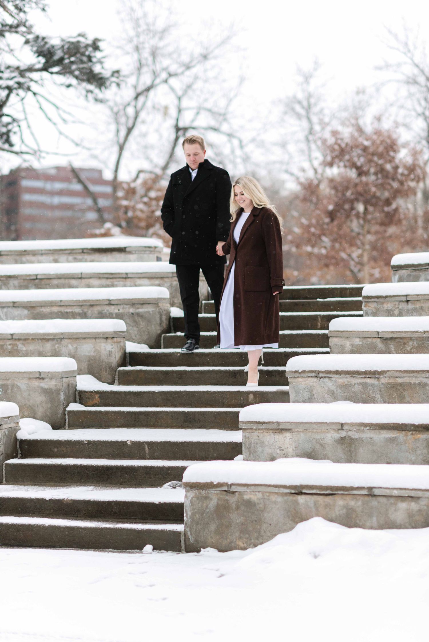 A couple stands on snowy concrete steps during winter.