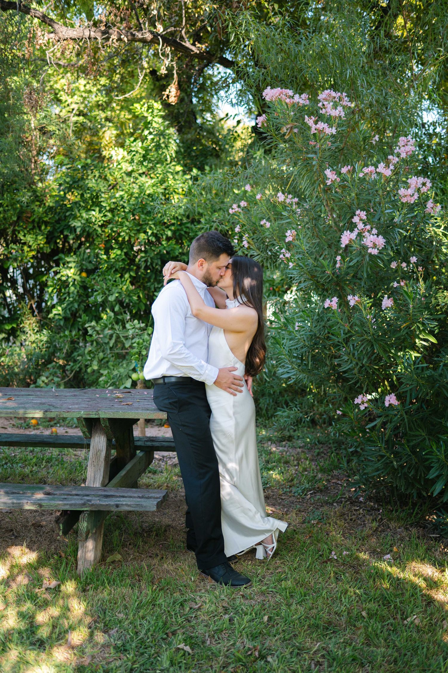 A romantic couple embraces in a lush garden setting with blooming flowers and wooden benches.