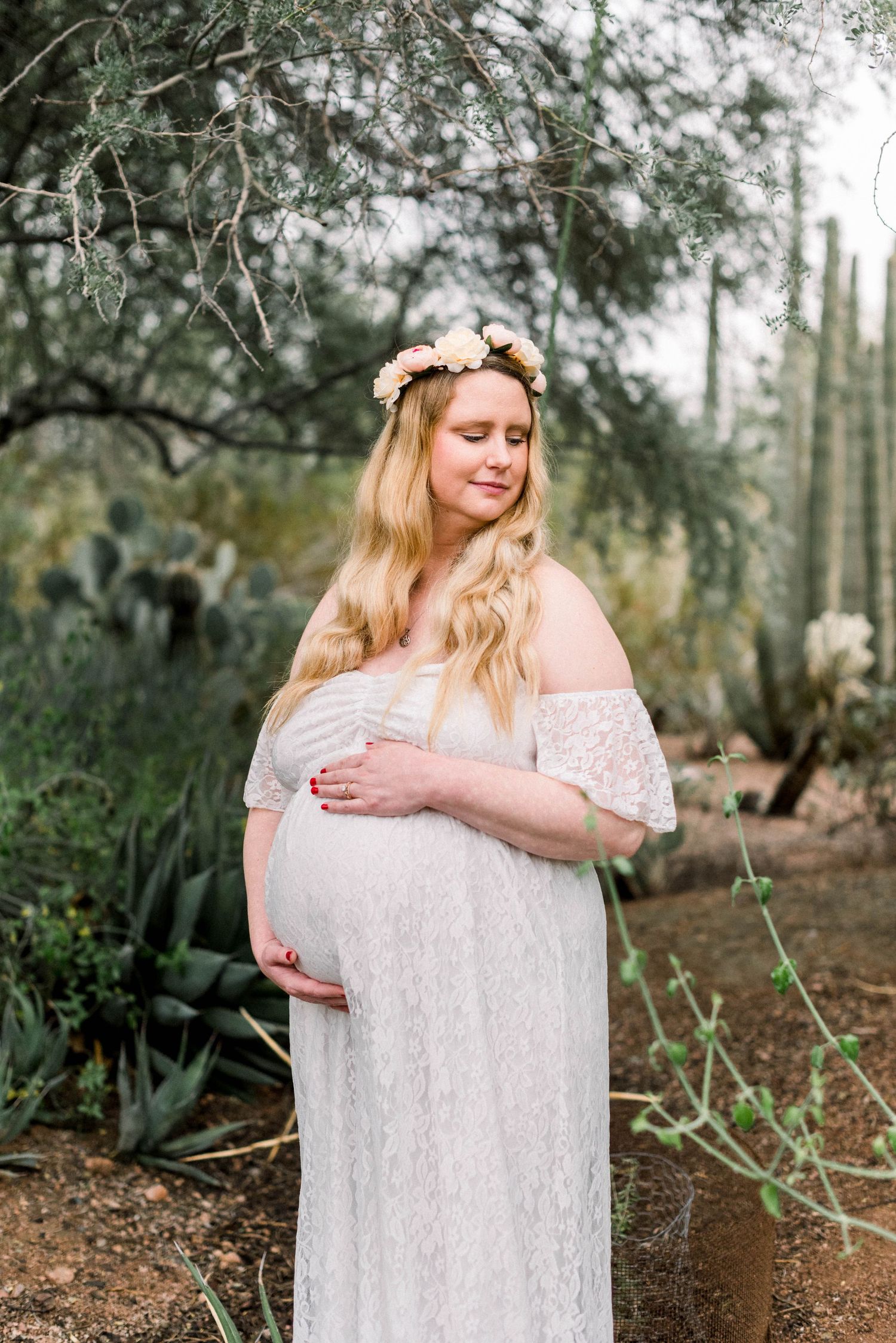 Romantic maternity photo featuring a white lace gown against desert flora backdrop.