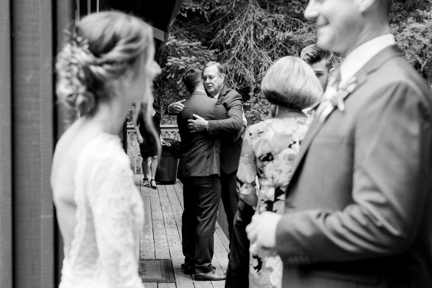 Black and white candid photo of wedding guests gathered on a deck.