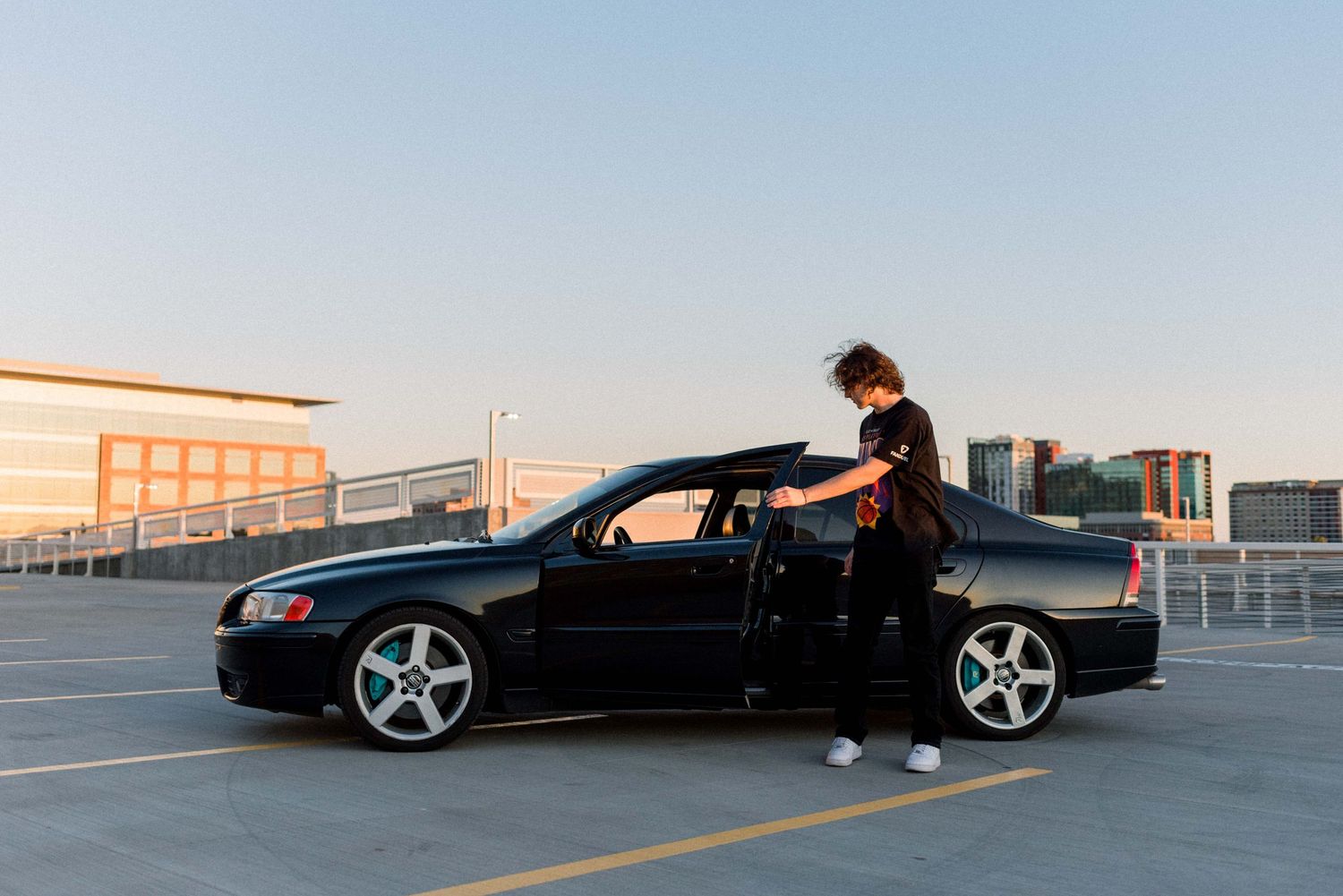 Person stepping out of black car in rooftop parking lot at sunset.