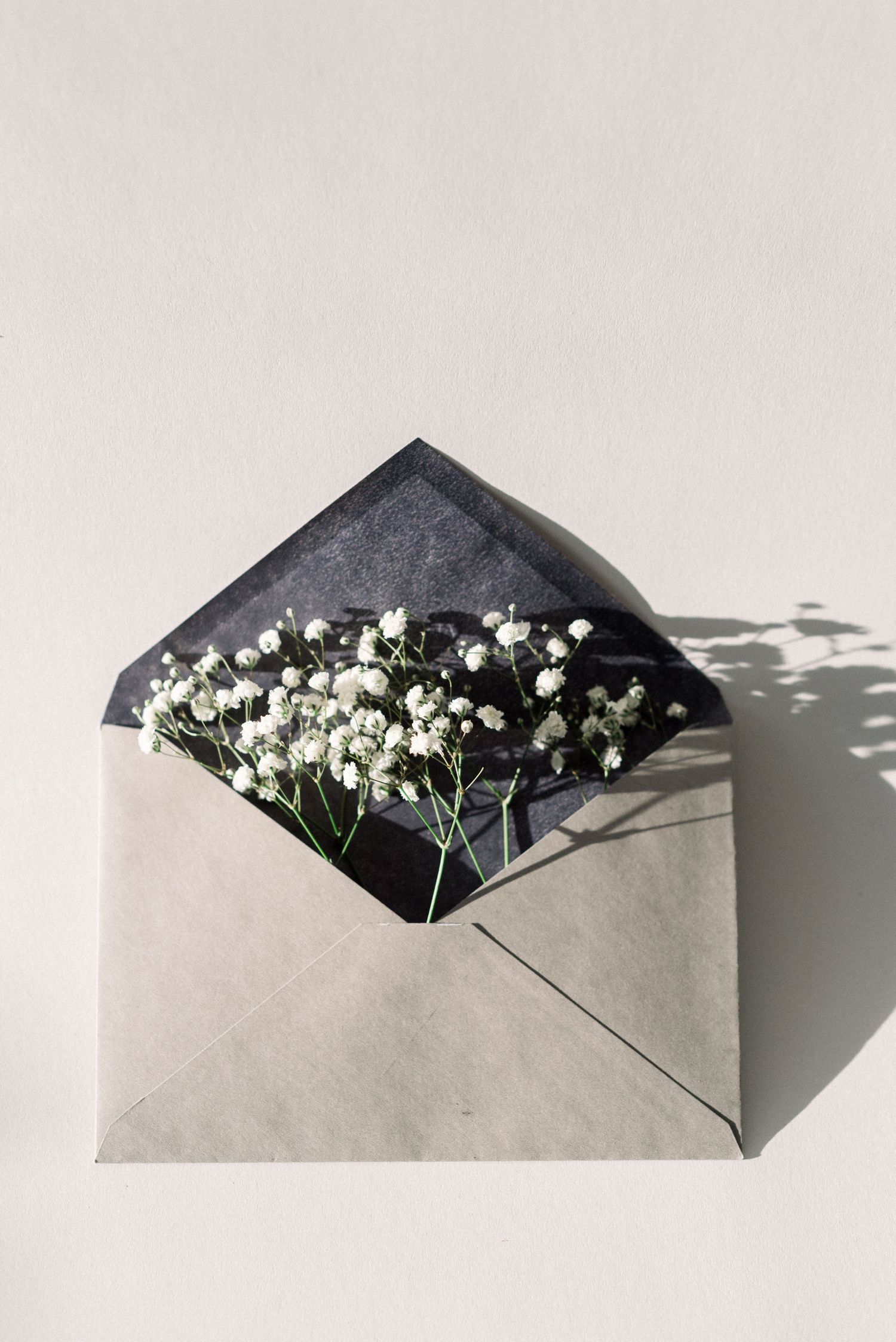 Gray envelope filled with delicate baby's breath flowers casting shadows on white surface.