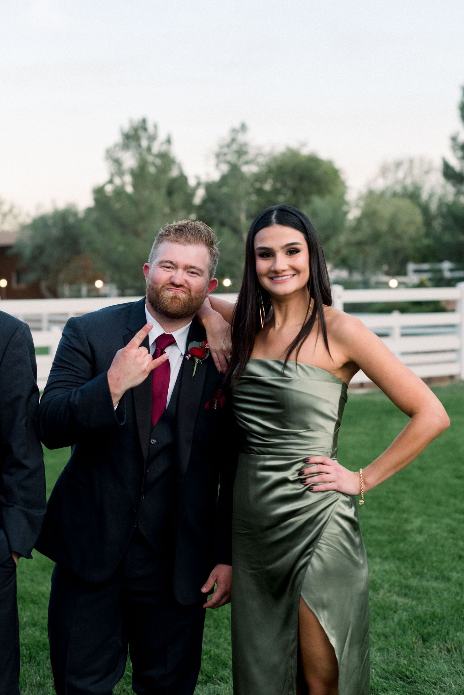 Wedding guests in formal attire posing together on lawn with white fencing in background.