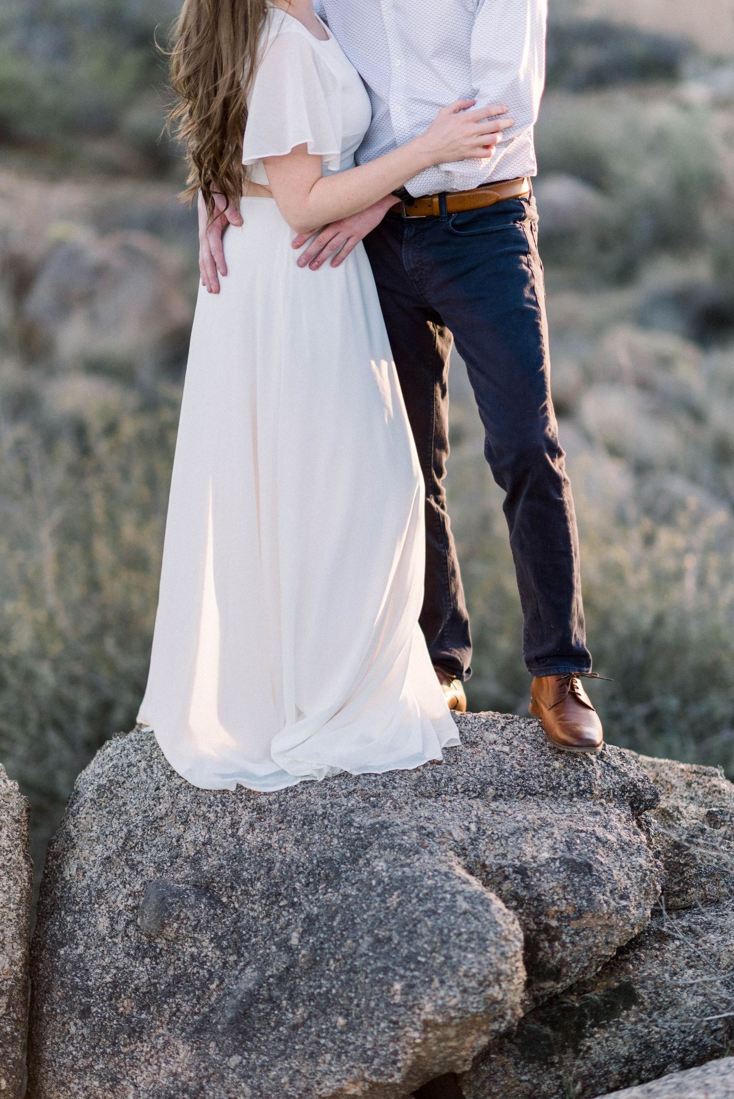 Romantic desert photoshoot on large rocks with flowing white dress and casual styling.